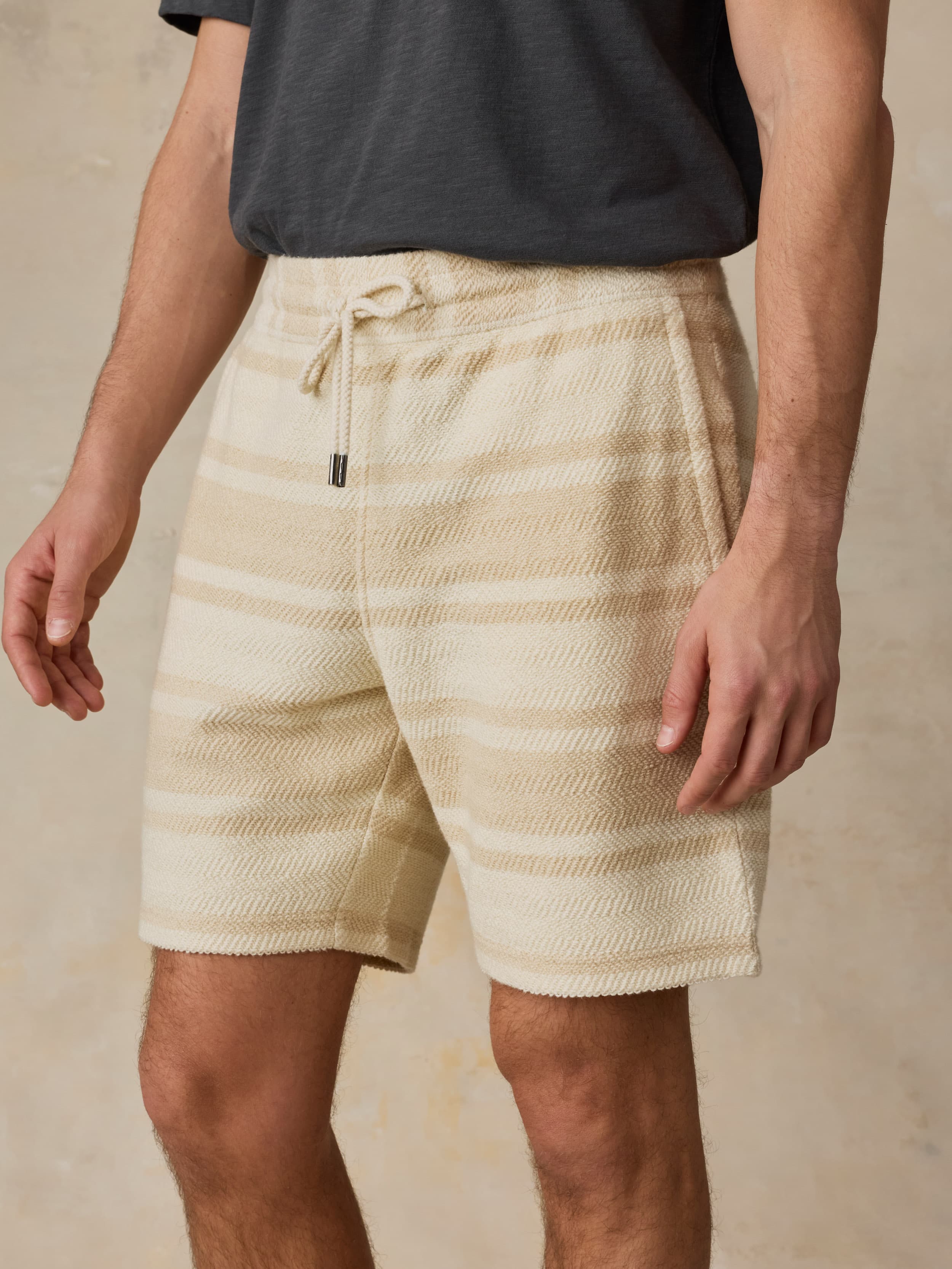 Man wearing beige striped shorts and a dark shirt against a neutral background