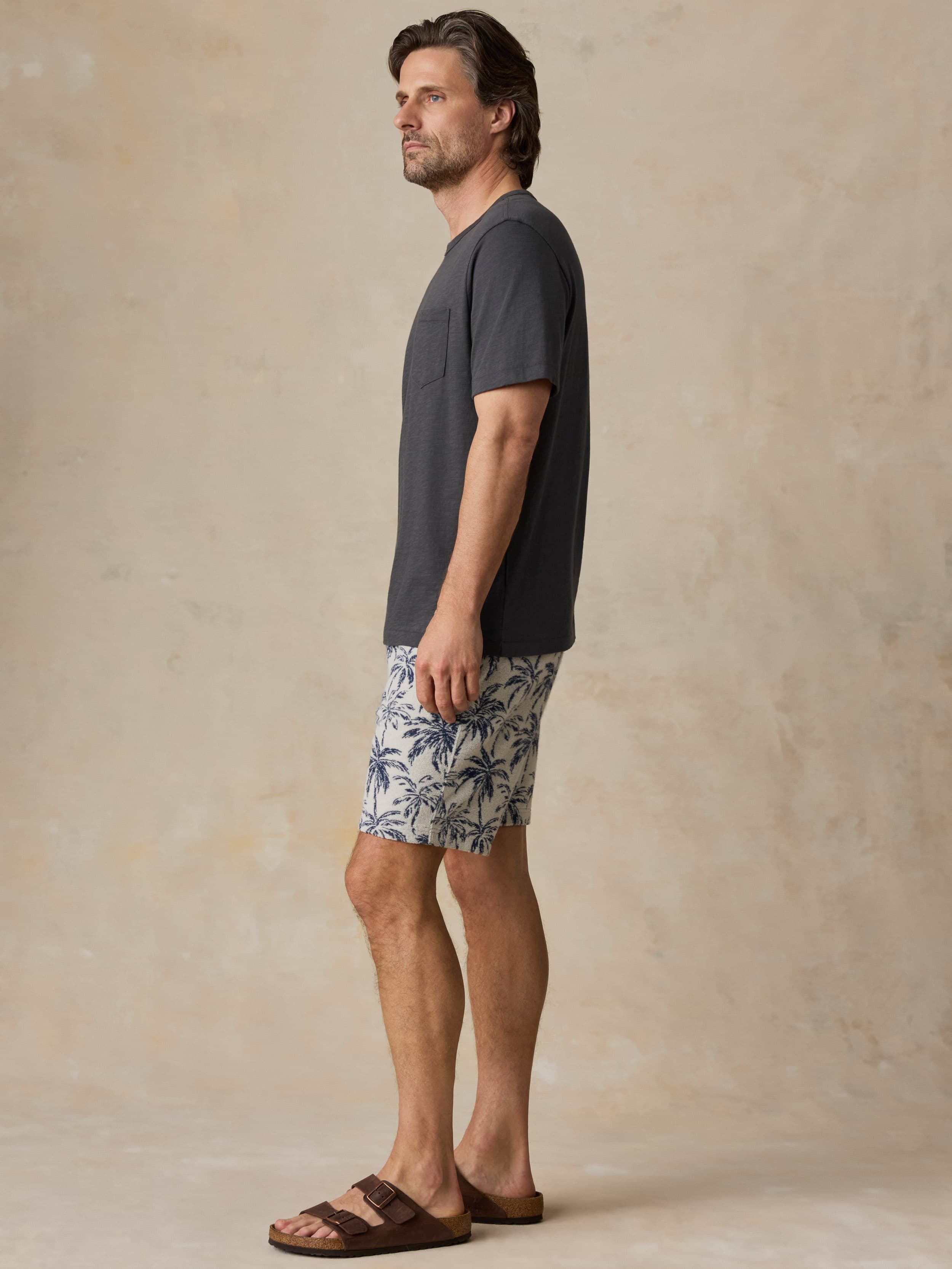 Man wearing a grey t-shirt and tropical printed shorts against a beige background