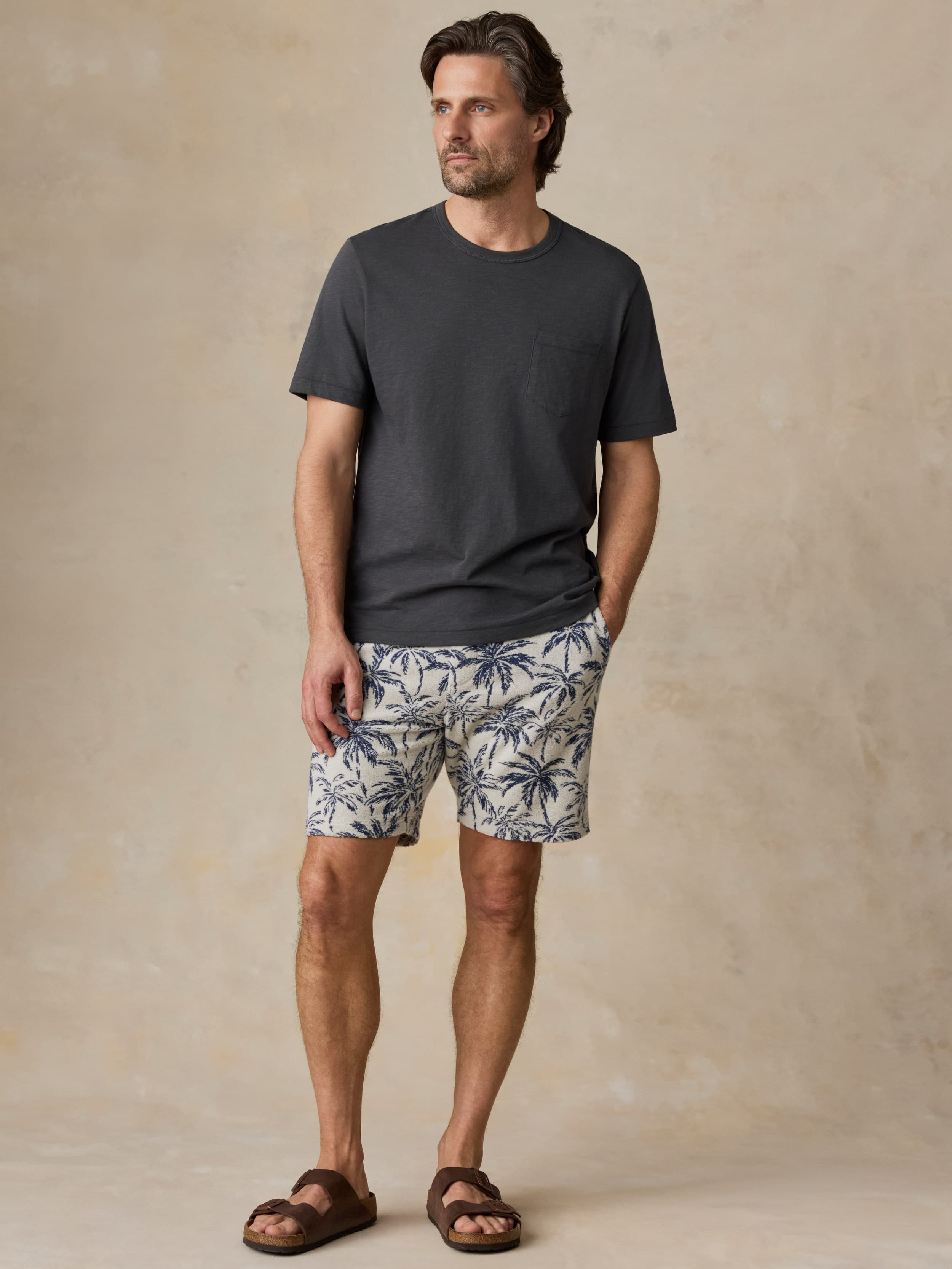Man wearing a grey t-shirt and tropical printed shorts against a beige background