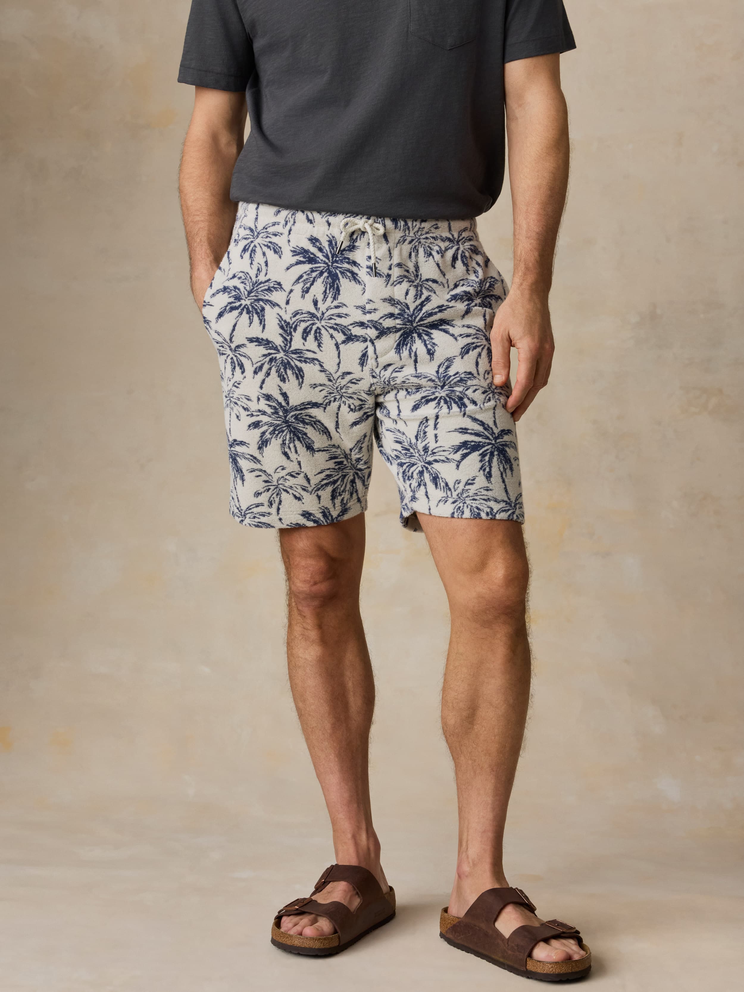 Man wearing a grey t-shirt and tropical printed shorts against a beige background