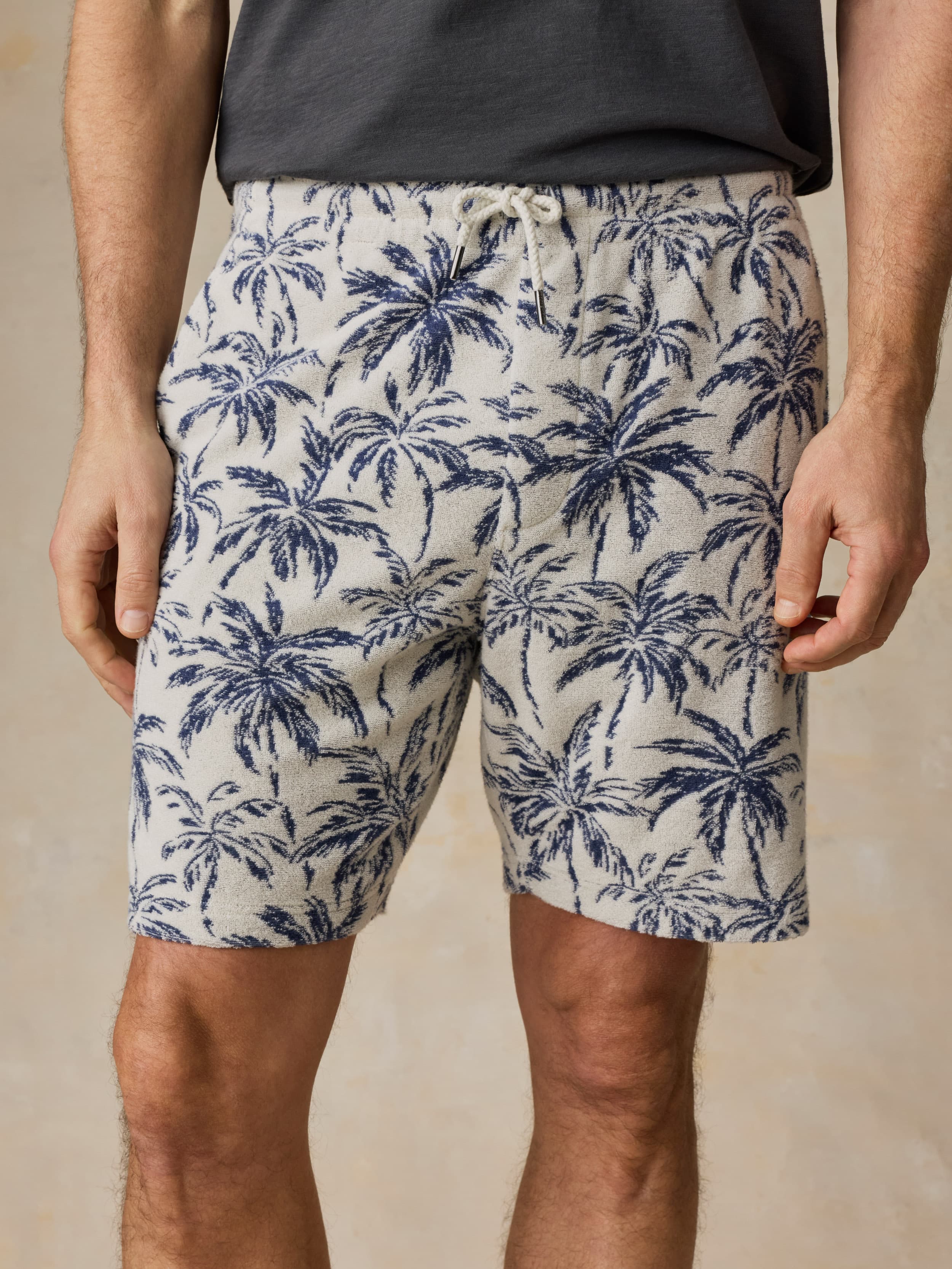 Man wearing a grey t-shirt and tropical printed shorts against a beige background