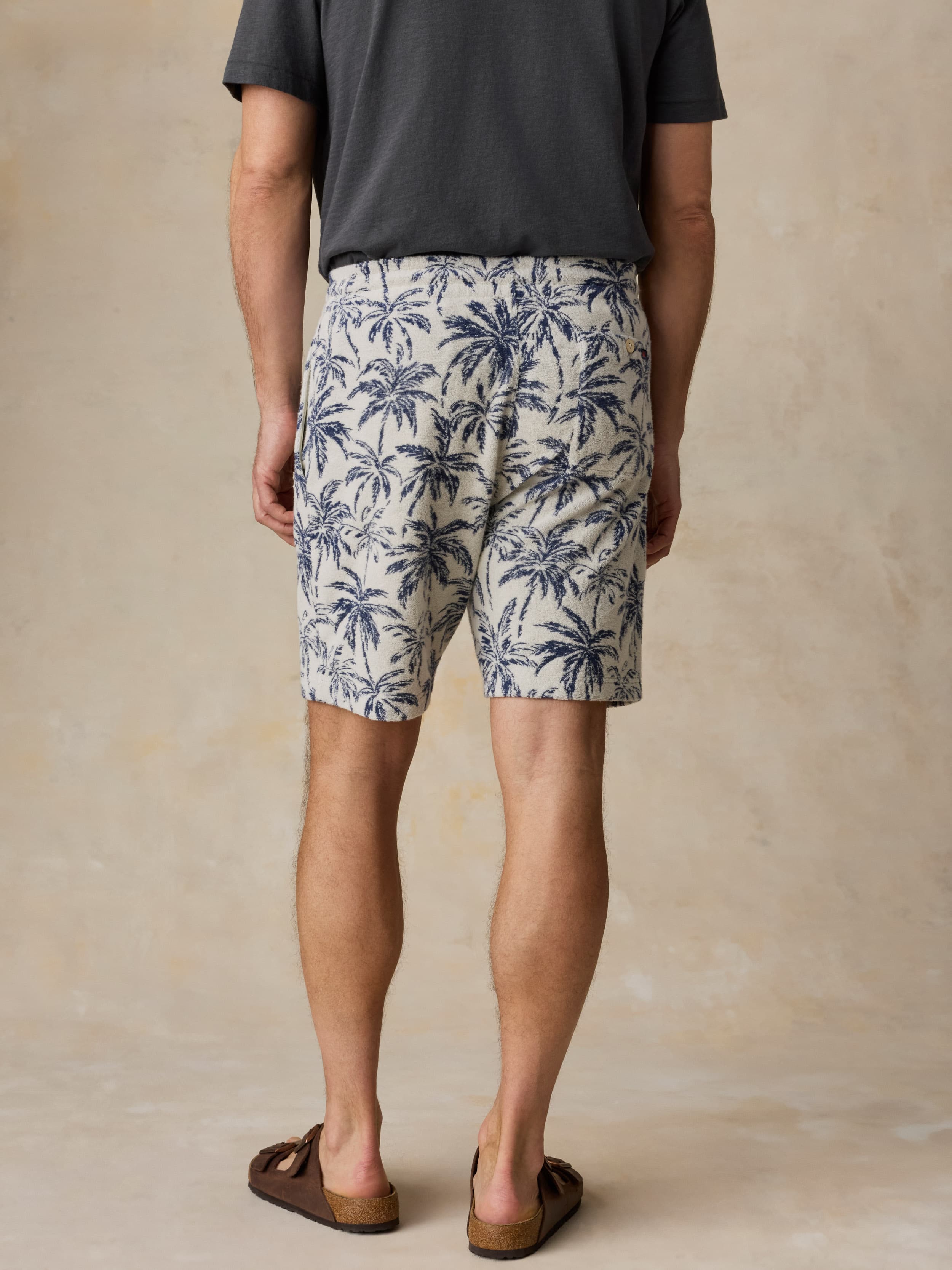 Man wearing a grey t-shirt and tropical printed shorts against a beige background
