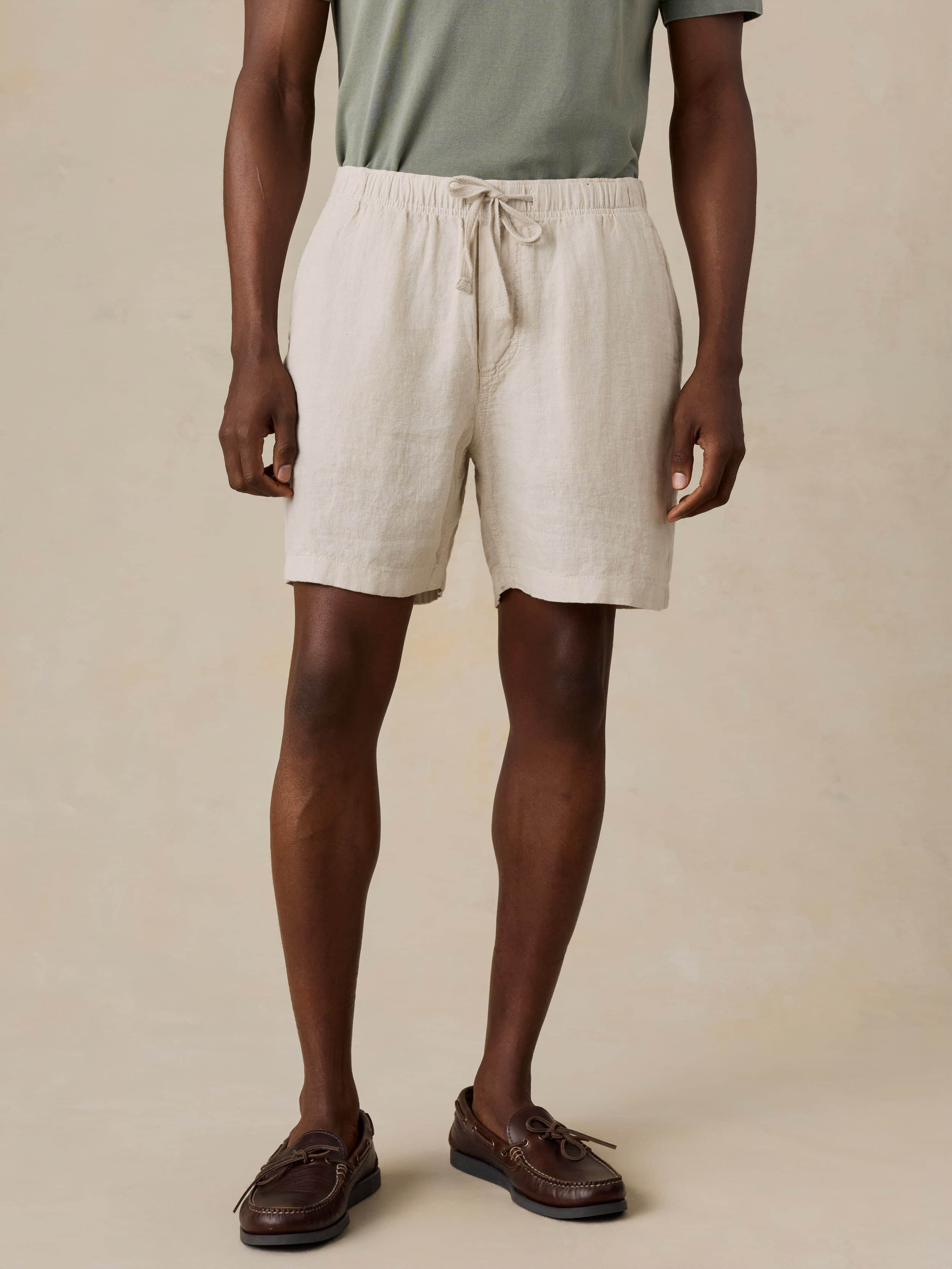 Man wearing a light green polo shirt and beige linen shorts against a beige background