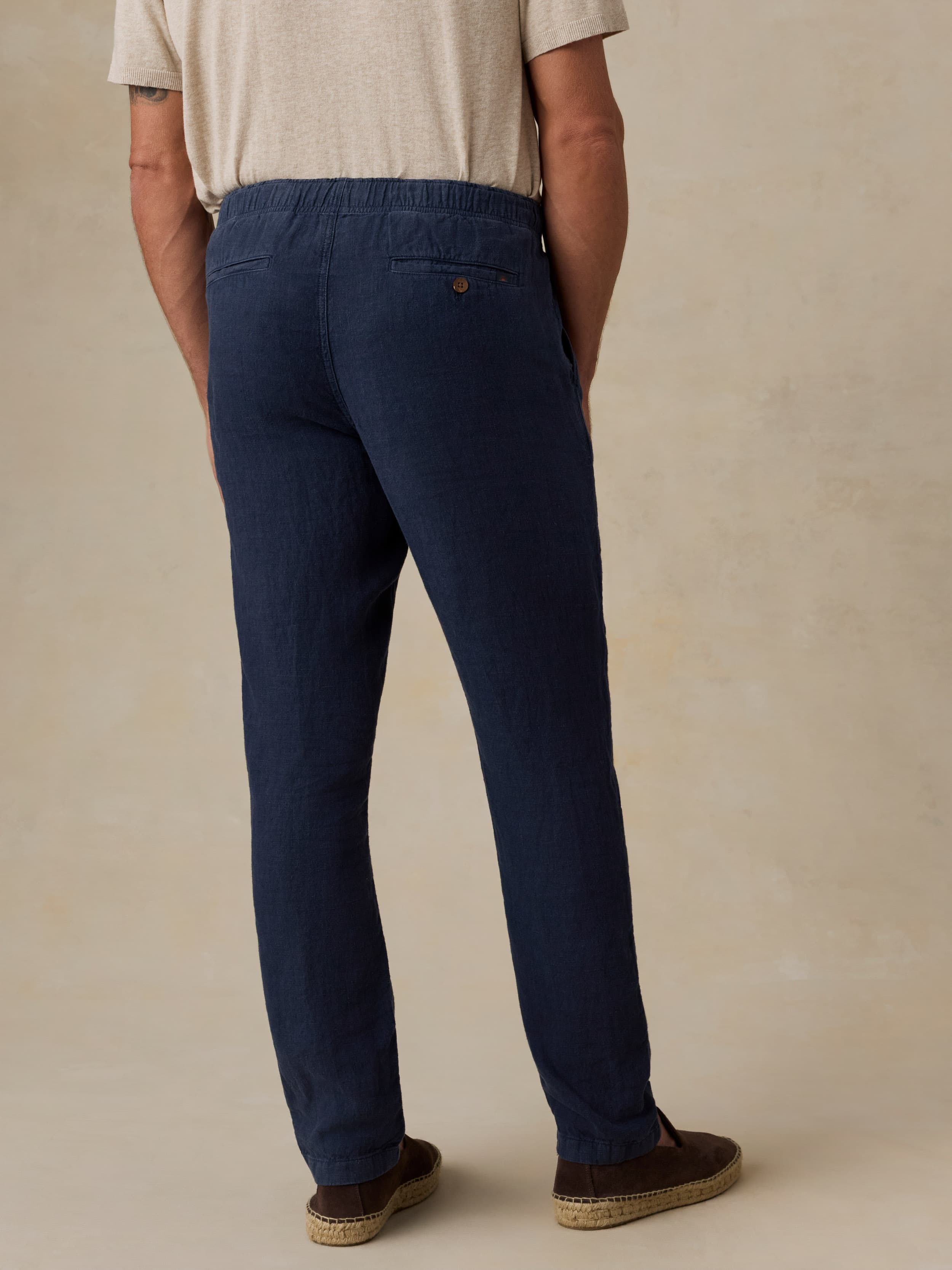 Man wearing navy linen pants against a beige background