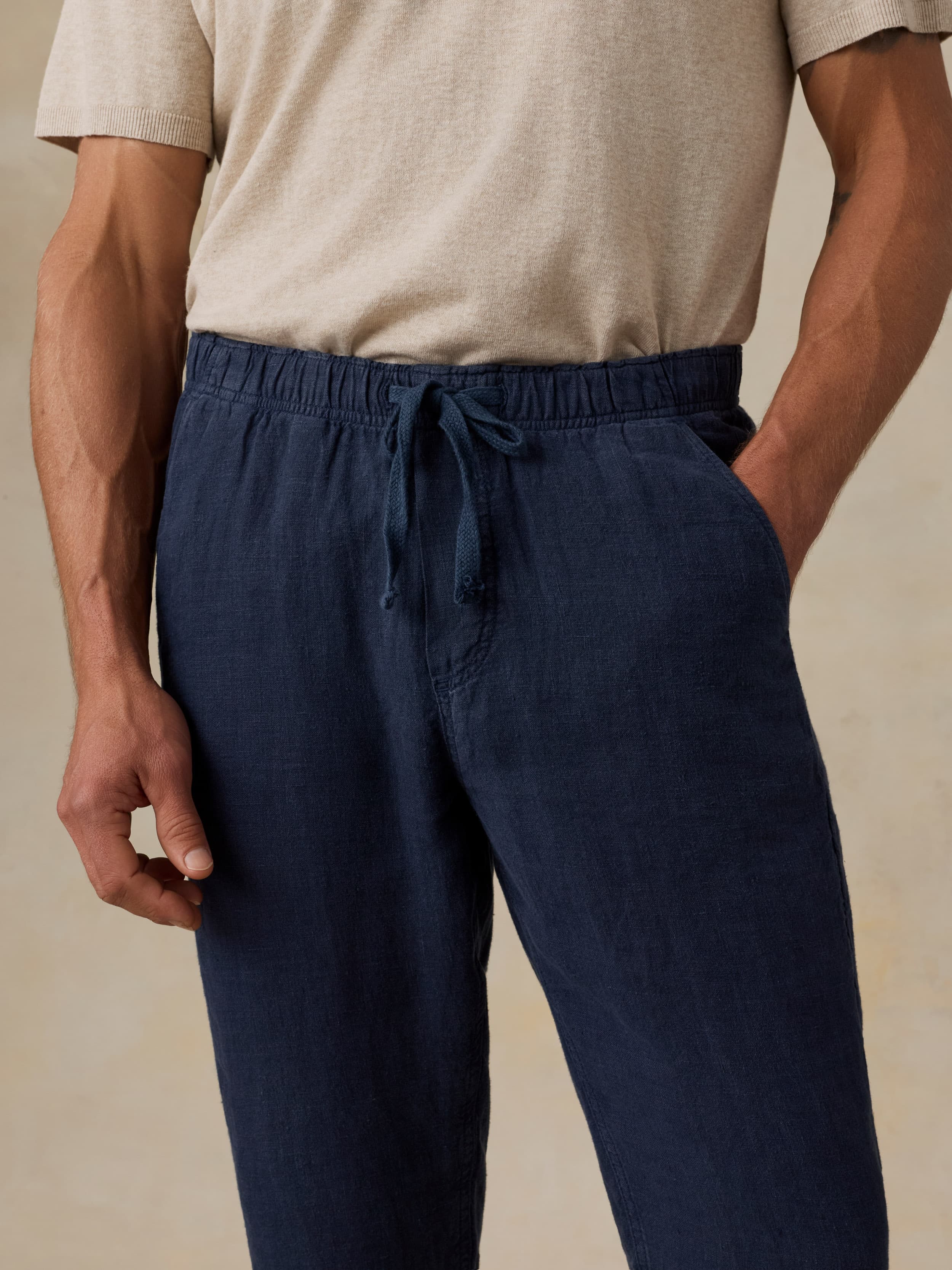 Man wearing navy linen pants and a beige shirt against a beige background