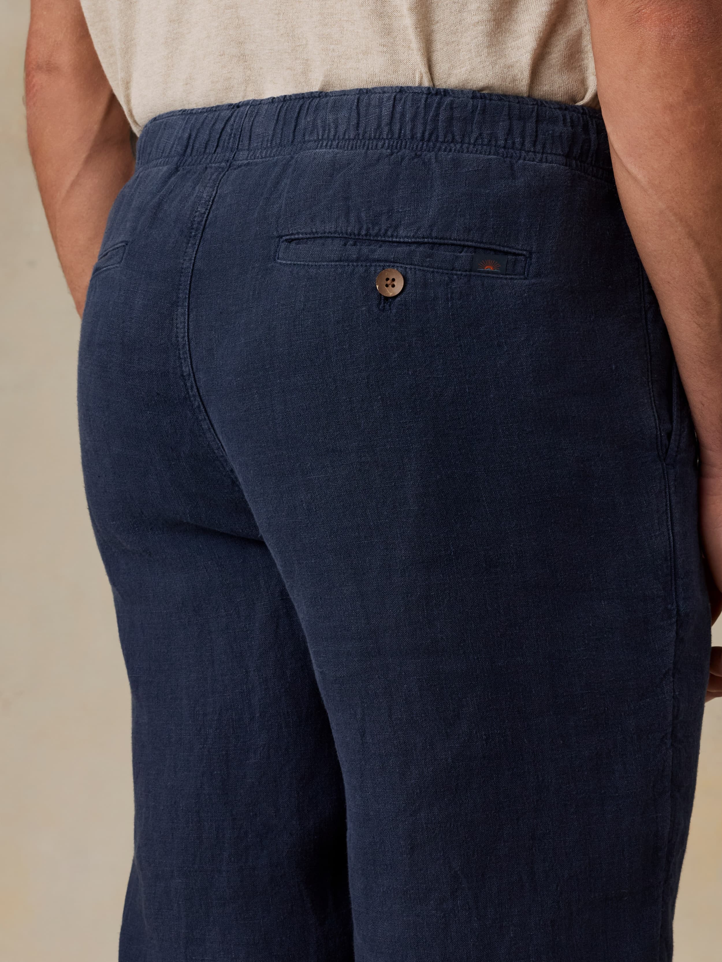 Man wearing navy linen pants against a beige background