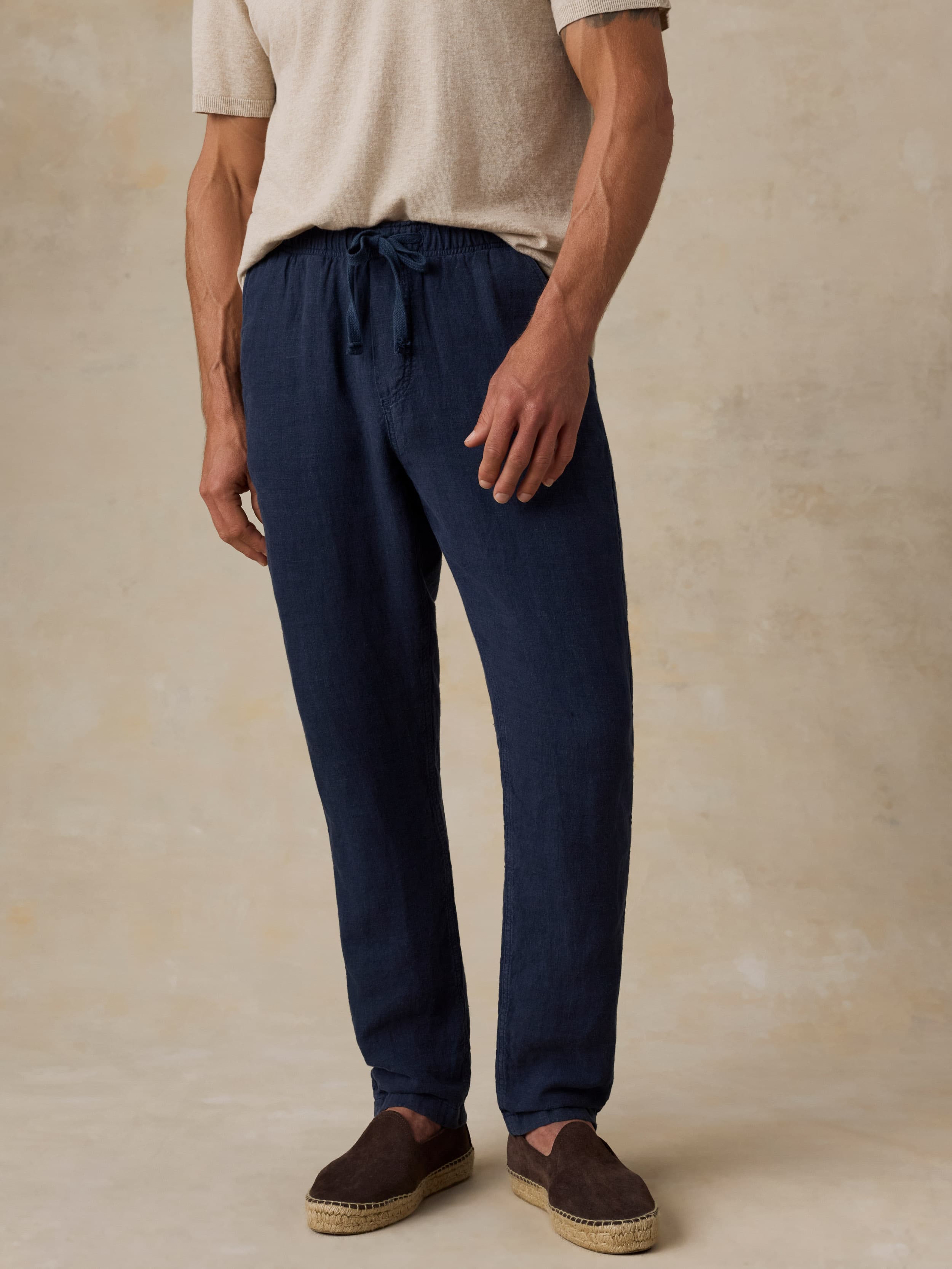 Man wearing navy linen pants and a beige t-shirt against a beige background