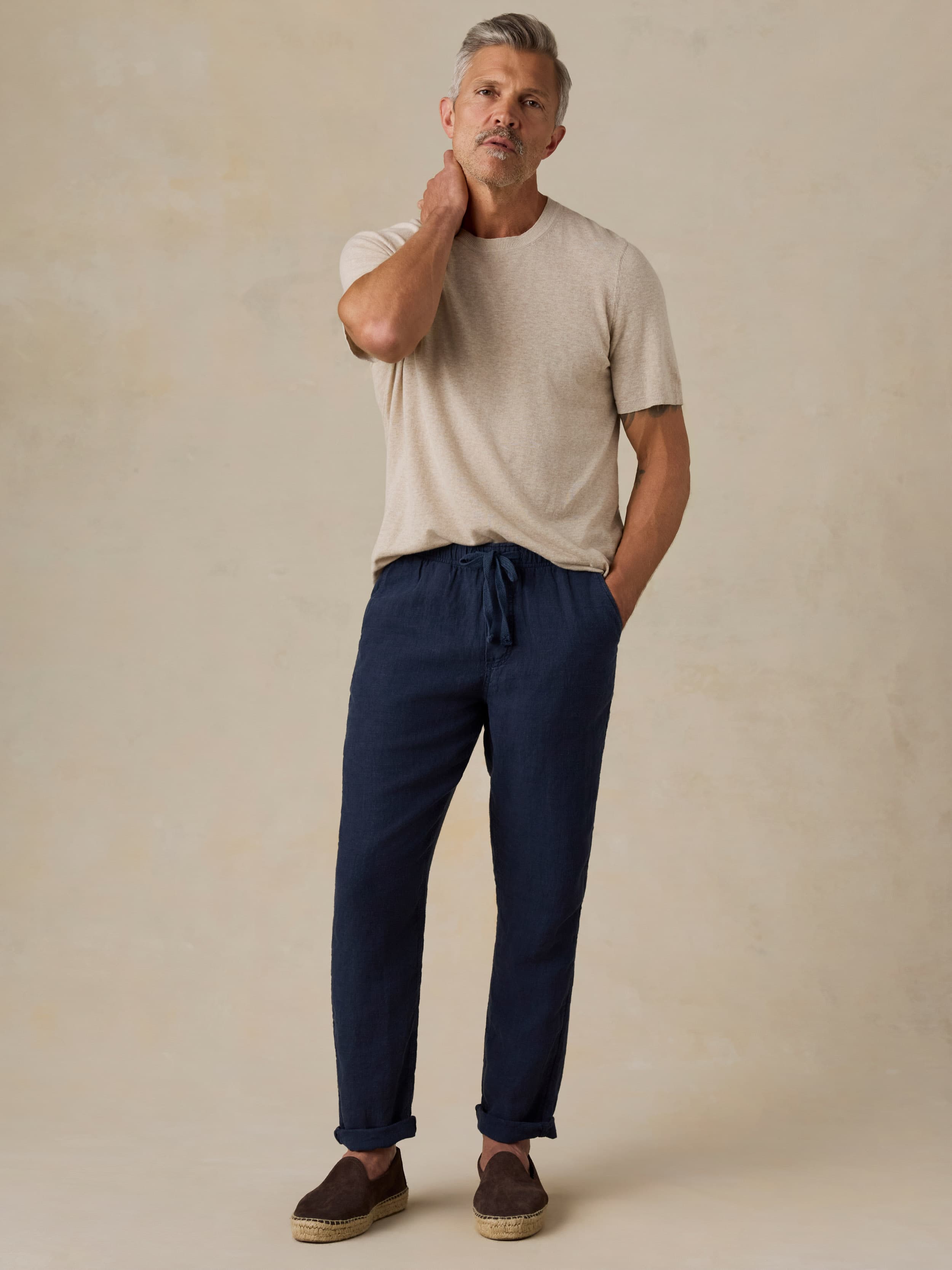 Man wearing navy linen pants and a beige t-shirt against a beige background