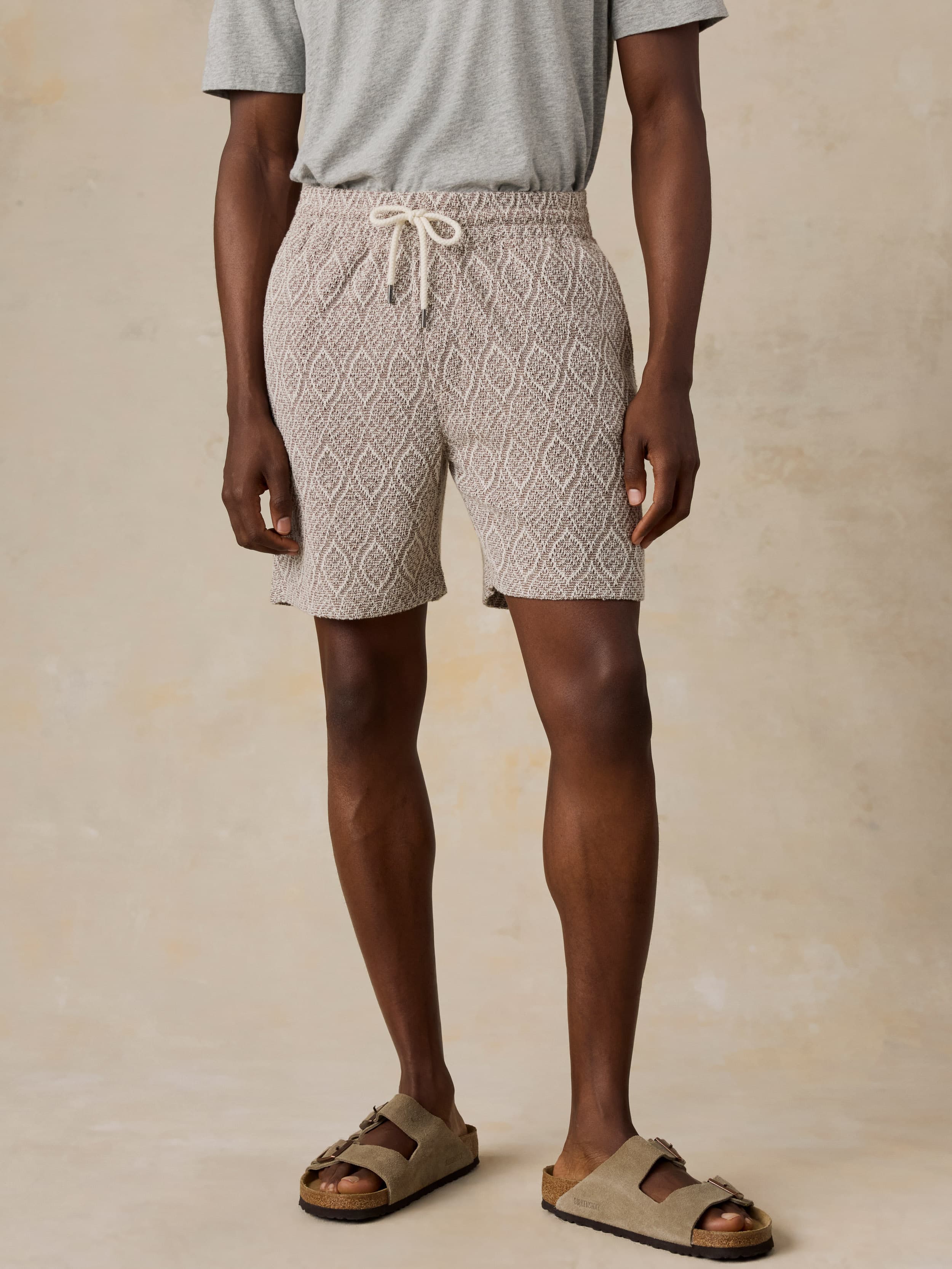 Man wearing brown printed shorts and a grey t-shirt against a beige background