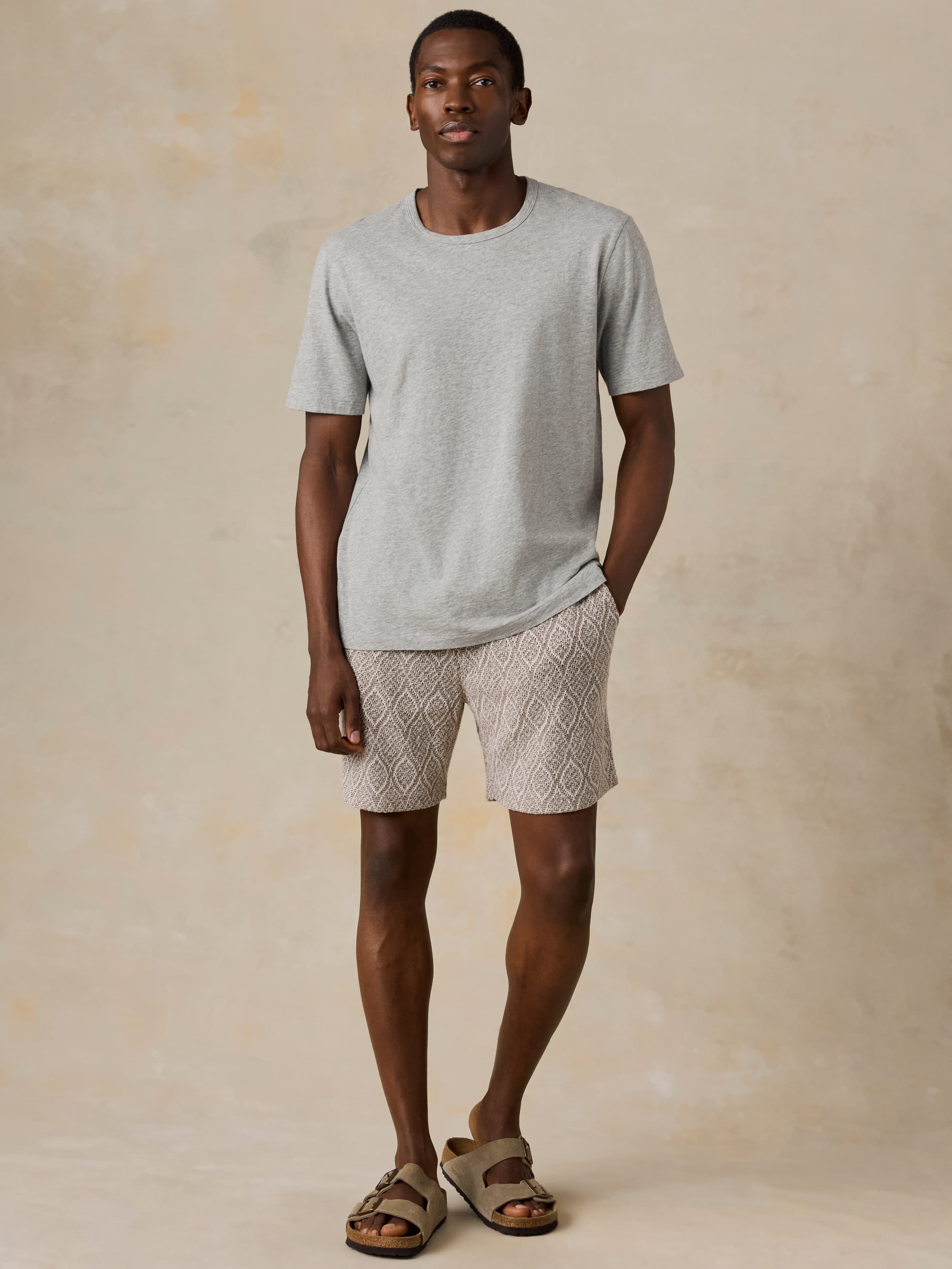 Man wearing brown printed shorts and a grey t-shirt against a beige background