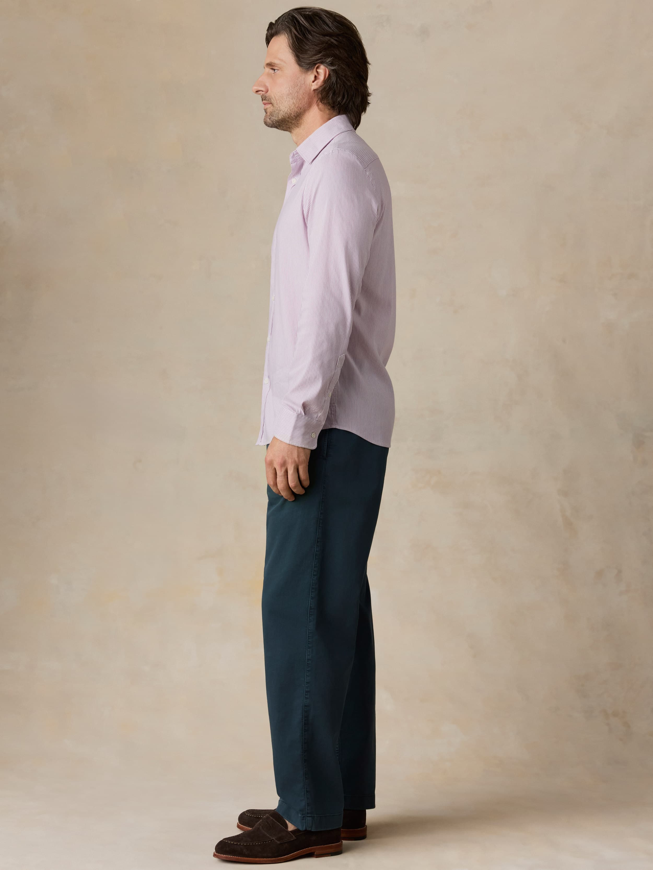 Man wearing navy pants with a purple button-down shirt against a beige background