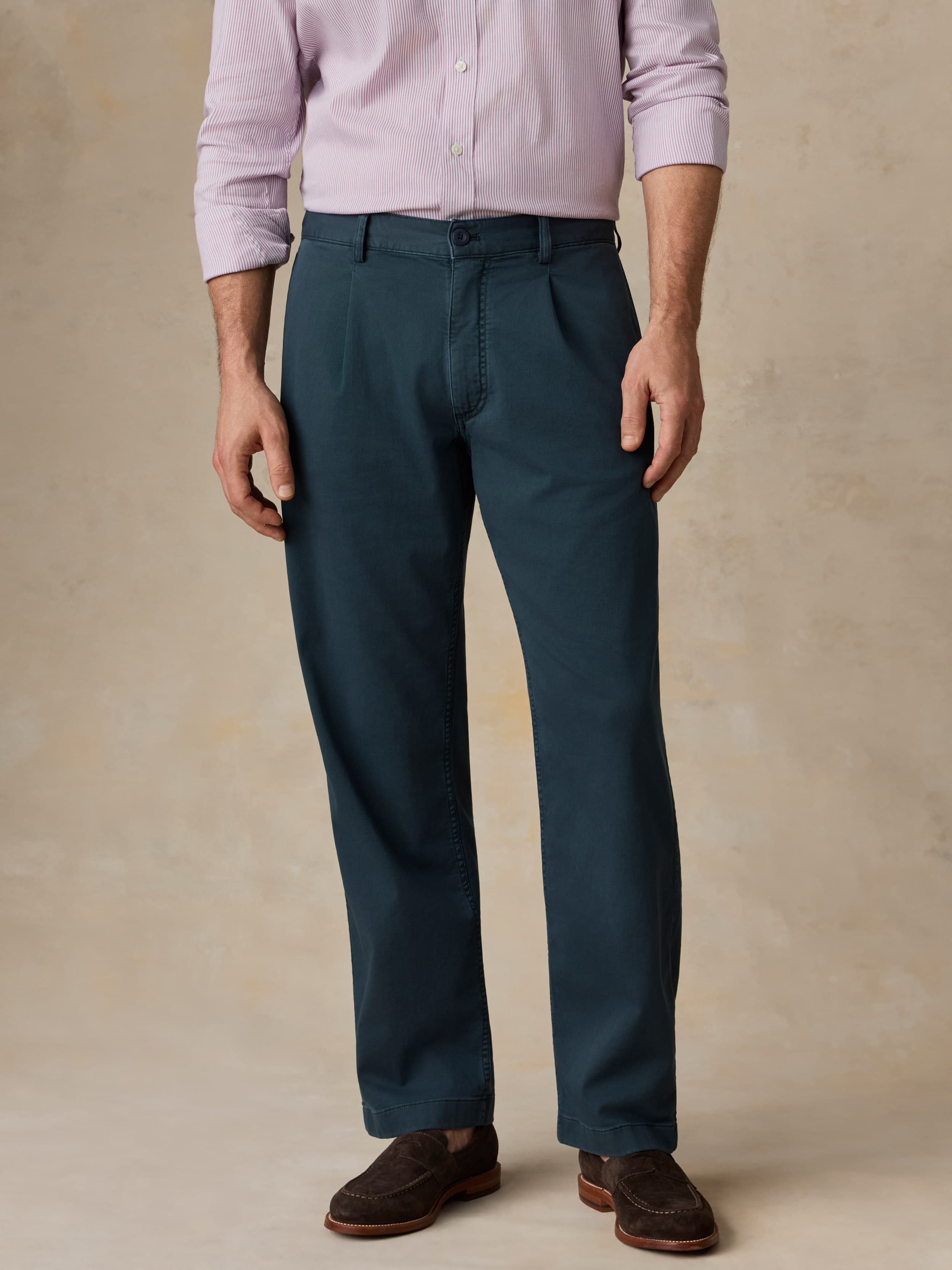 Man wearing navy pants with a purple button-down shirt against a beige background