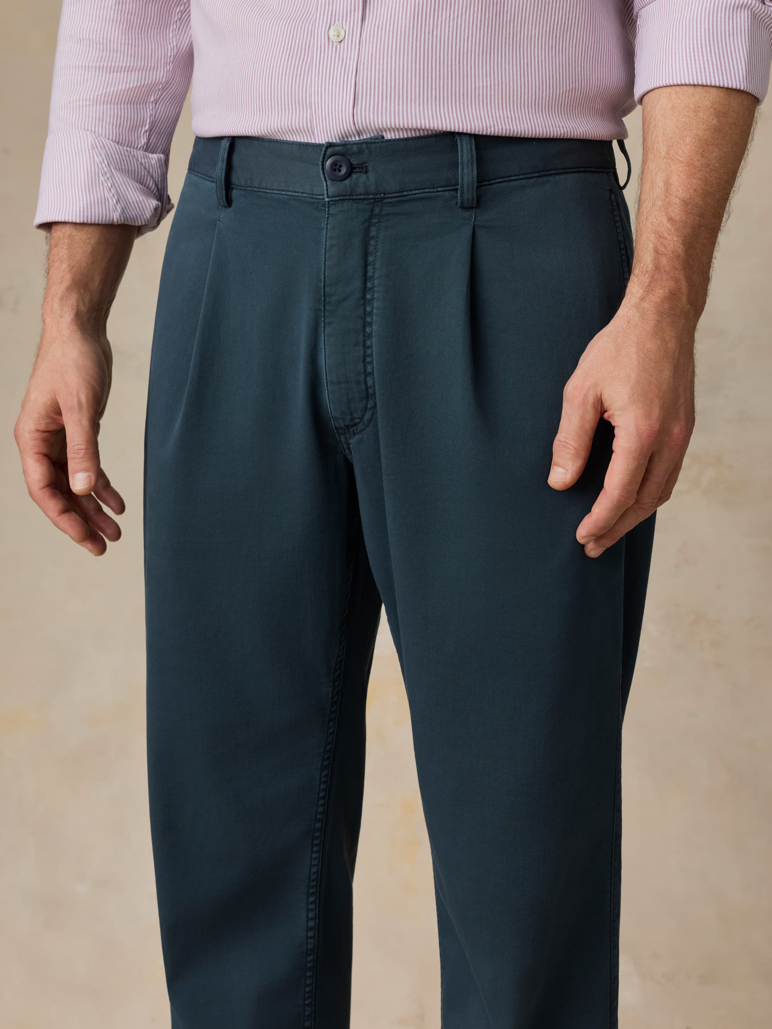 Man wearing navy pants with a purple button-down shirt against a beige background
