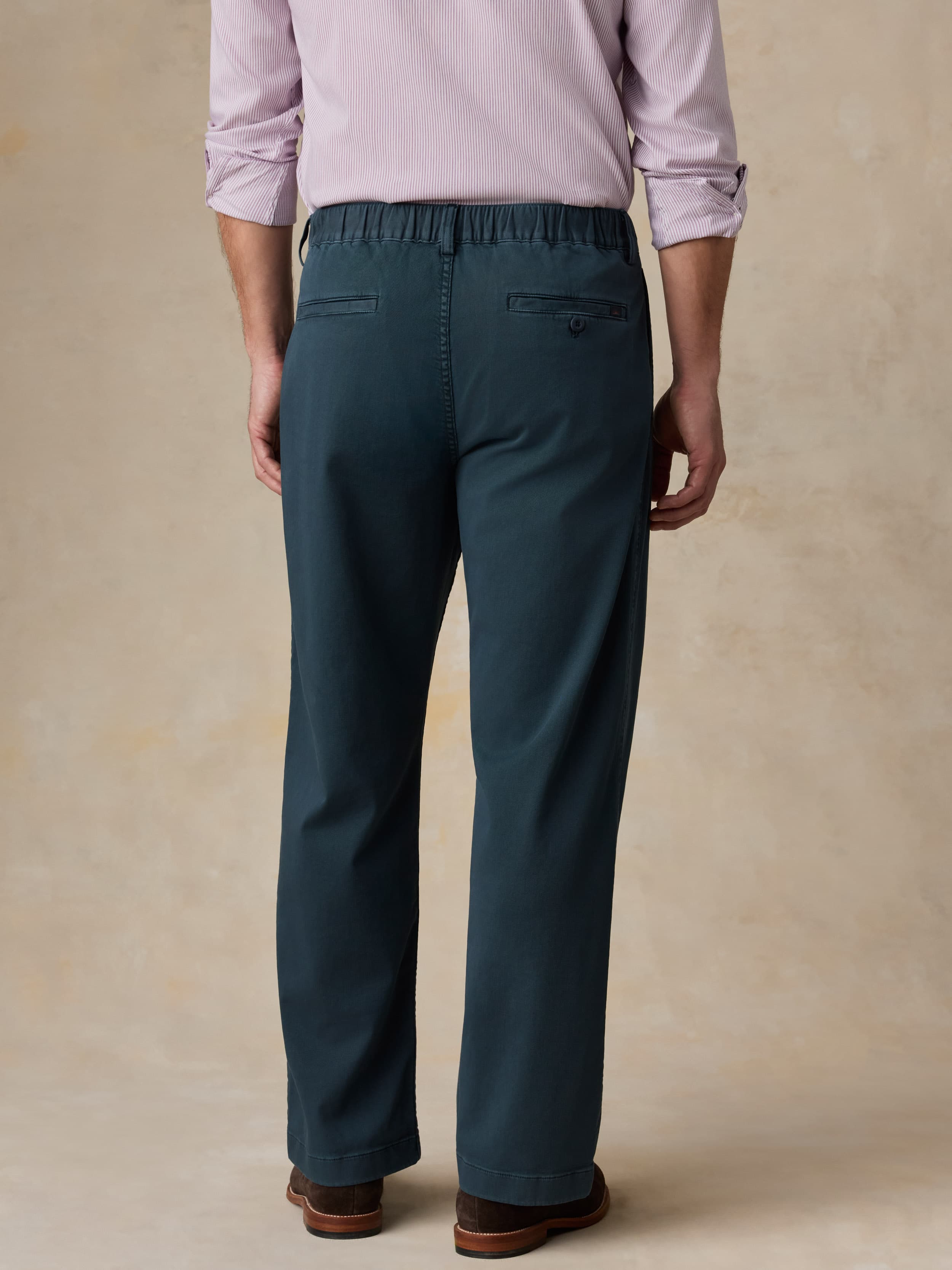Man wearing navy pants with a purple button-down shirt against a beige background