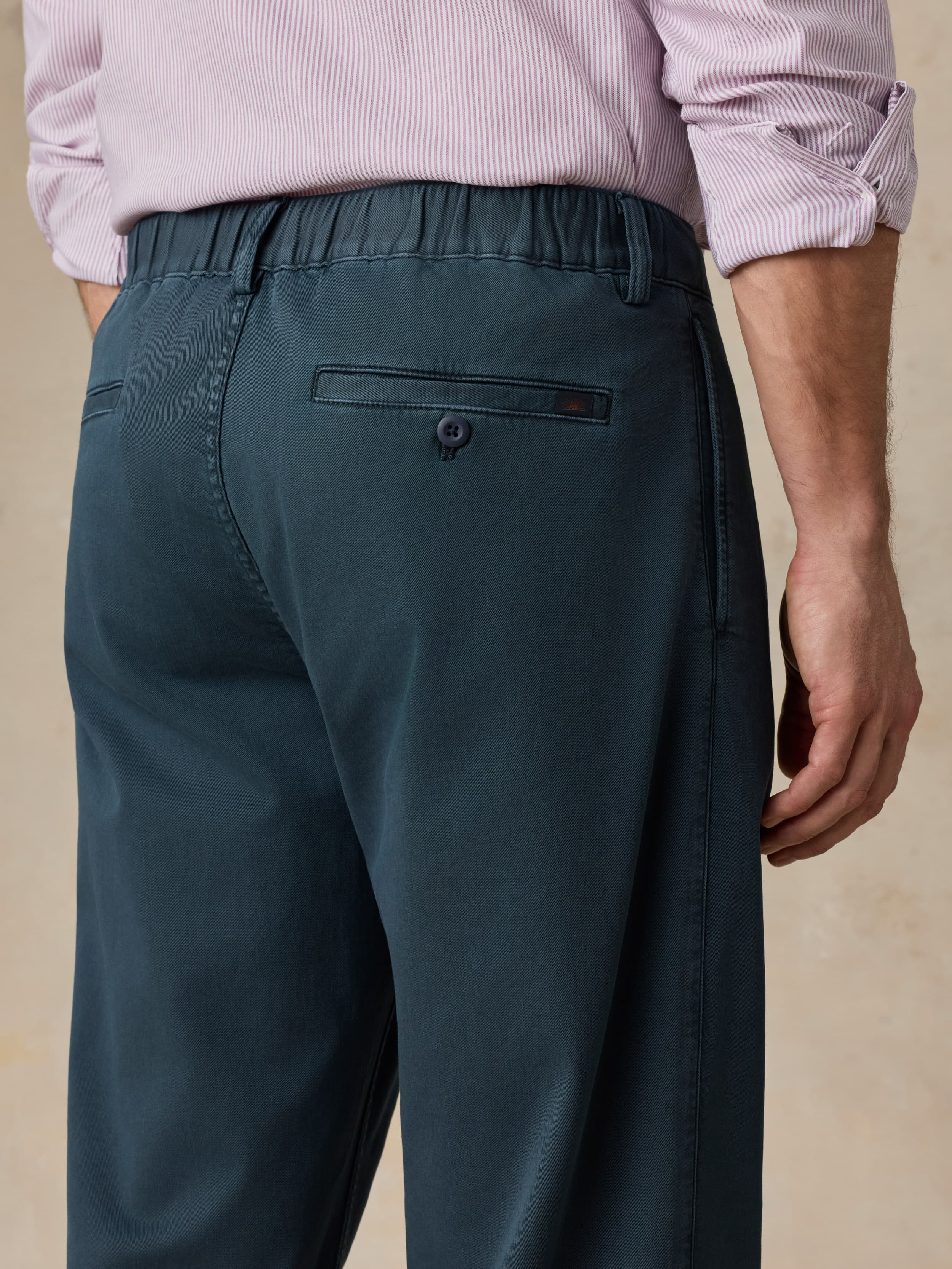 Man wearing navy pants with a purple button-down shirt against a beige background