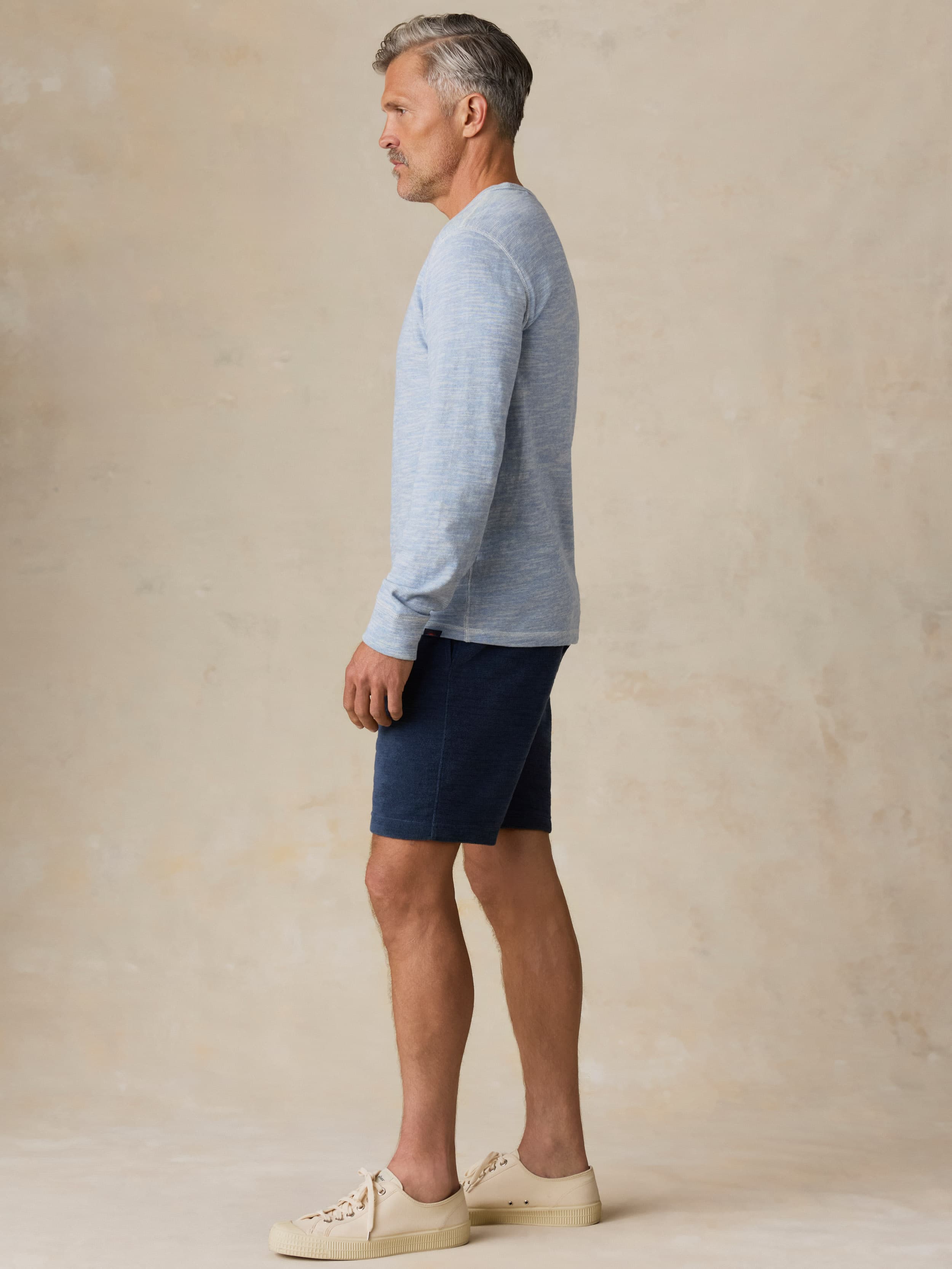 Man wearing a light blue crewneck and navy shorts against a beige background