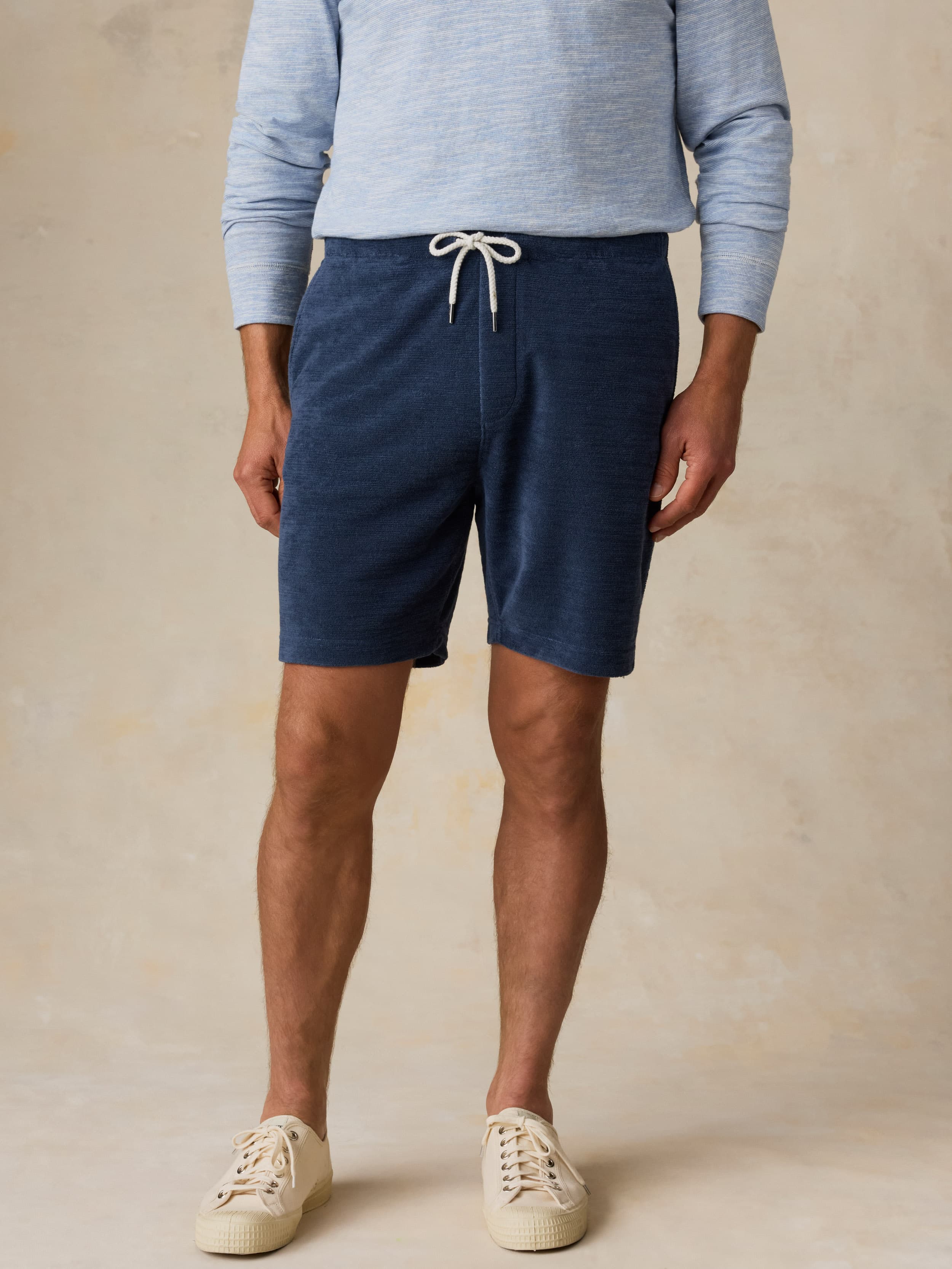 Man wearing a light blue crewneck and navy shorts against a beige background