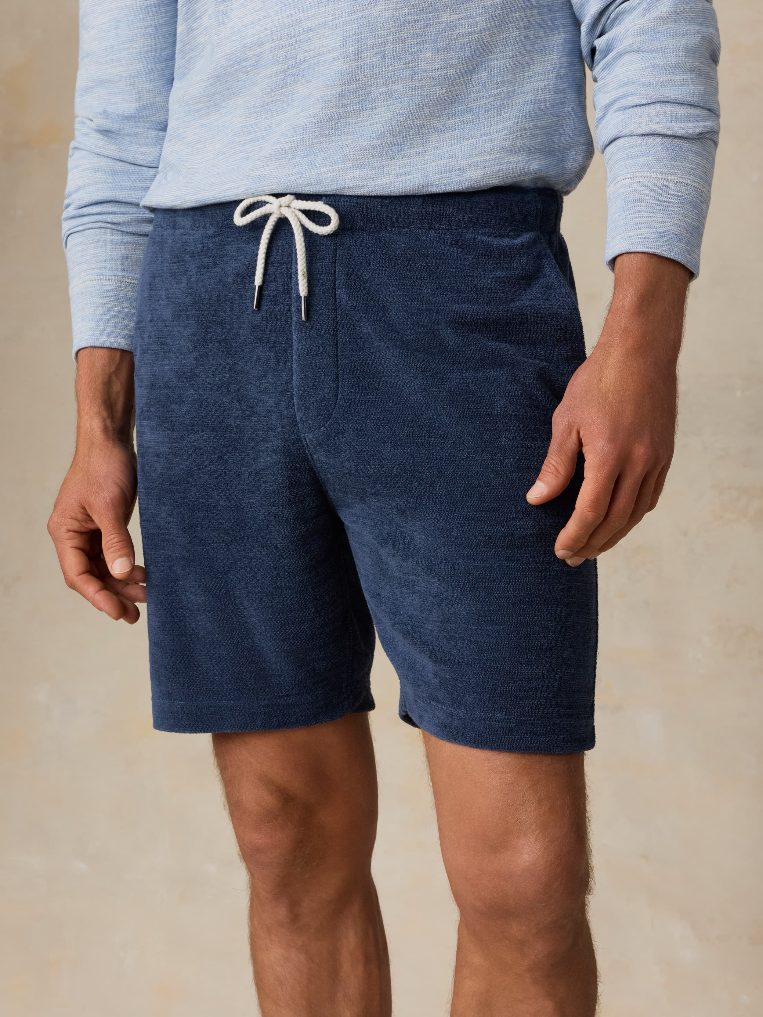 Man wearing a light blue crewneck and navy shorts against a beige background