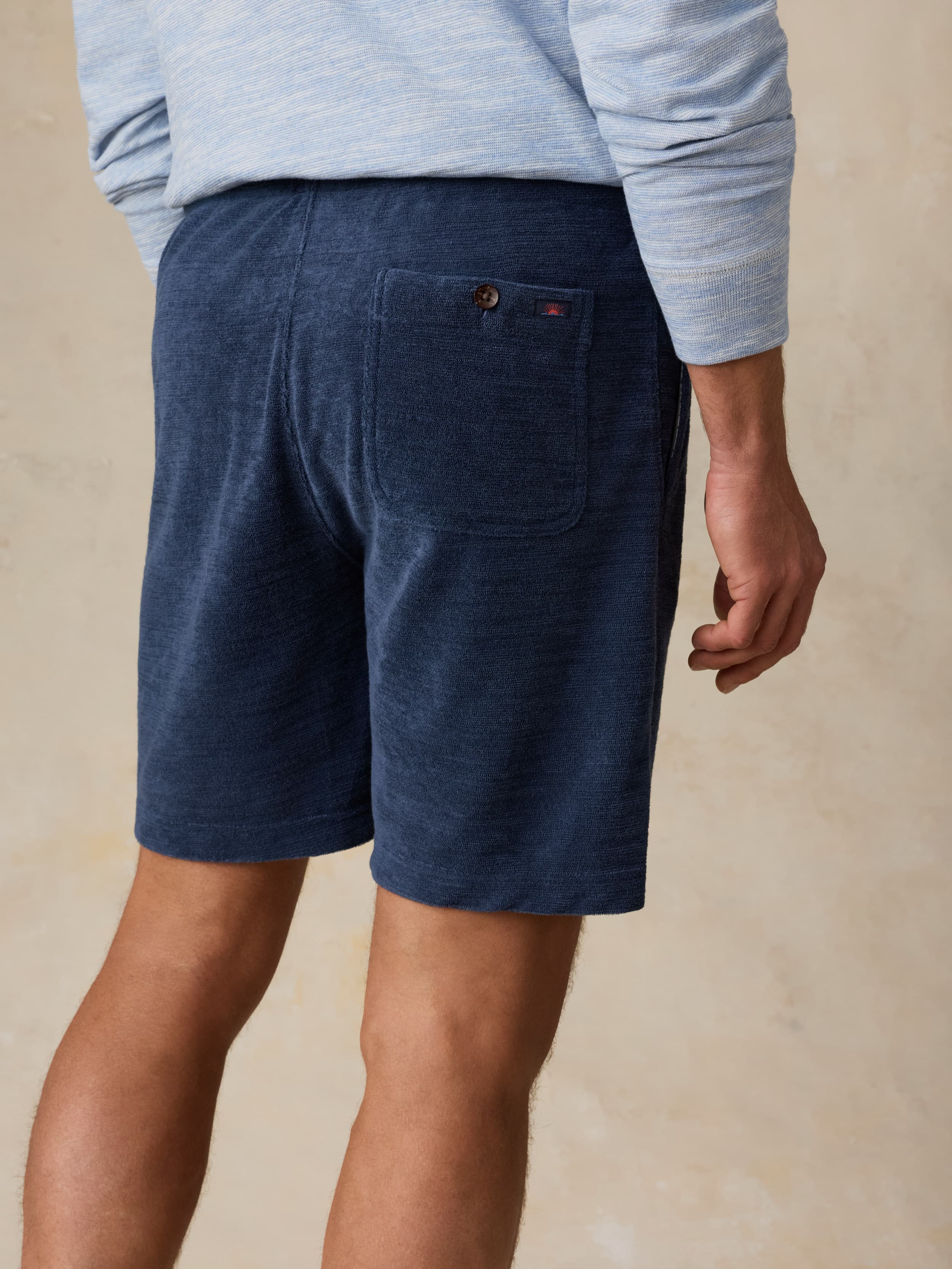 Man wearing a light blue crewneck and navy shorts against a beige background