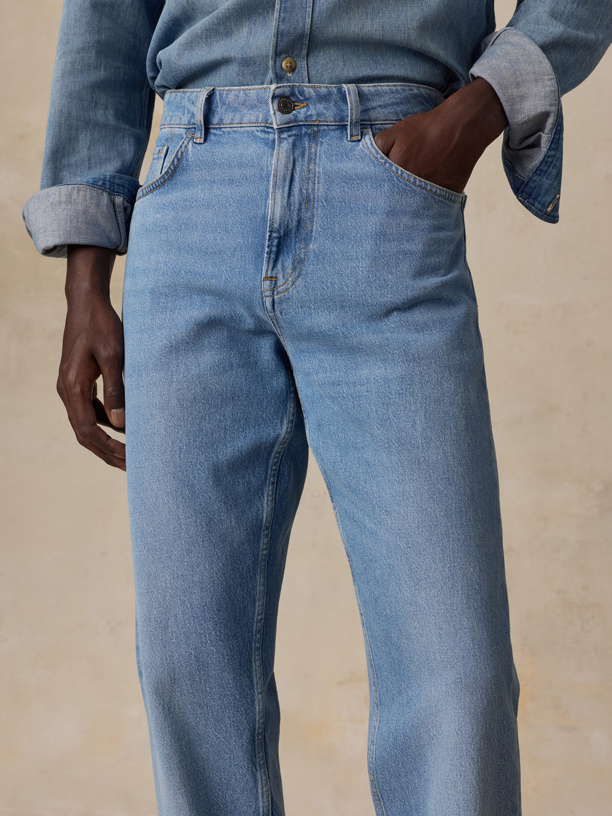 A close up of a man wearing a light blue denim shirt and matching light blue jeans, image 4 of 5