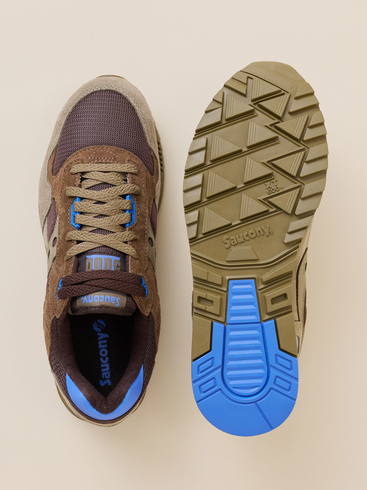 A pair of Saucony sneakers shown from above, with one shoe displaying the brown suede and mesh upper with blue accents, and the other showing the olive green and blue treaded outsole., image 4 of 4