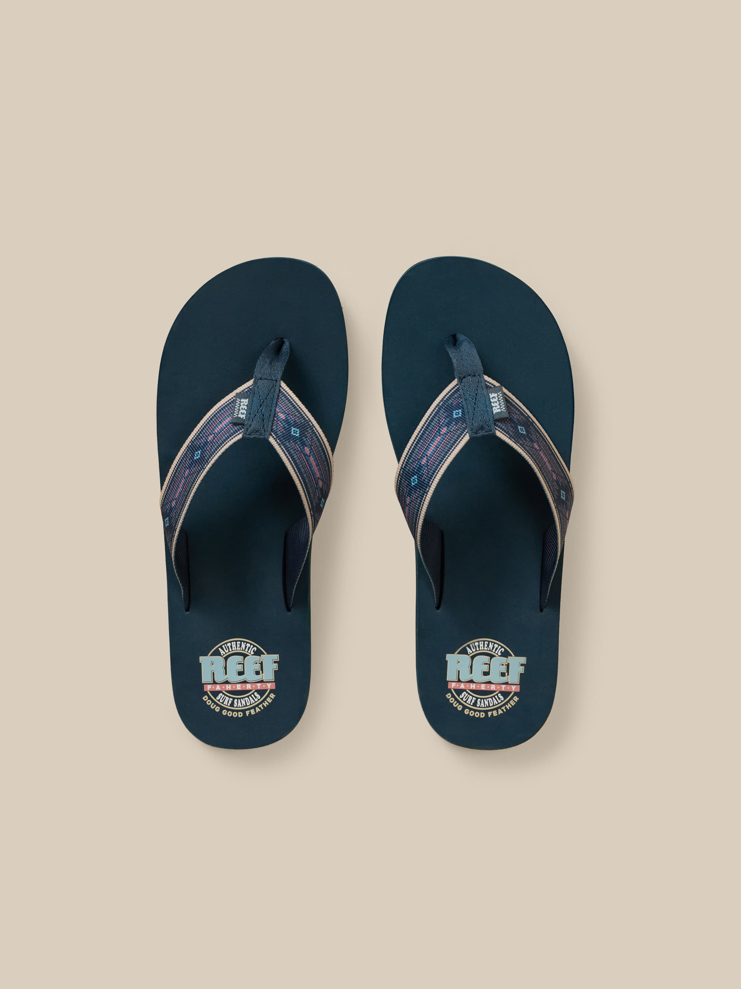 Pair of navy blue flip-flops with a Faherty x REEF brand logo on a beige background