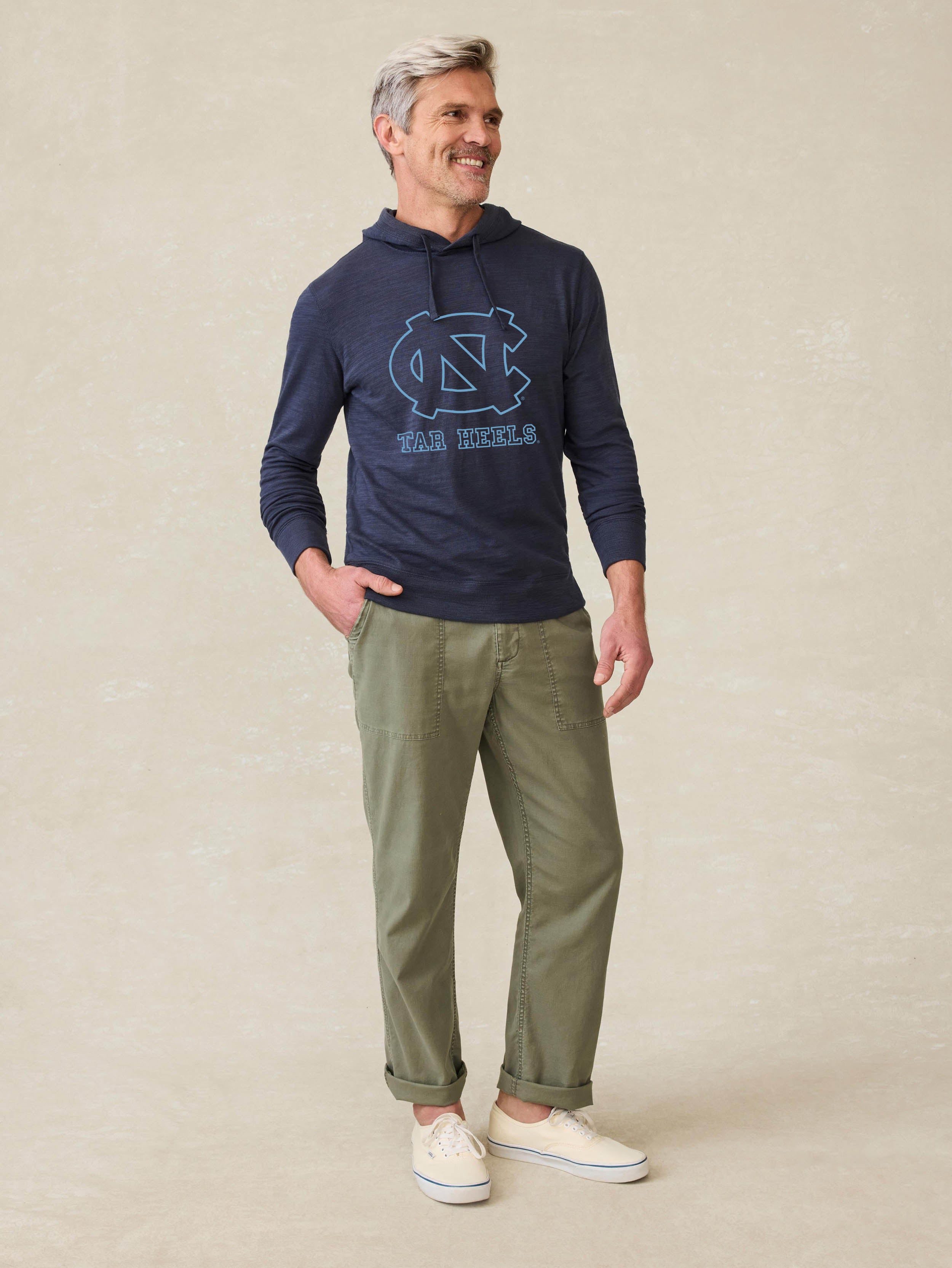 Man is wearing a navy blue hoodie with UNC graphic at the center chest against a beige background
