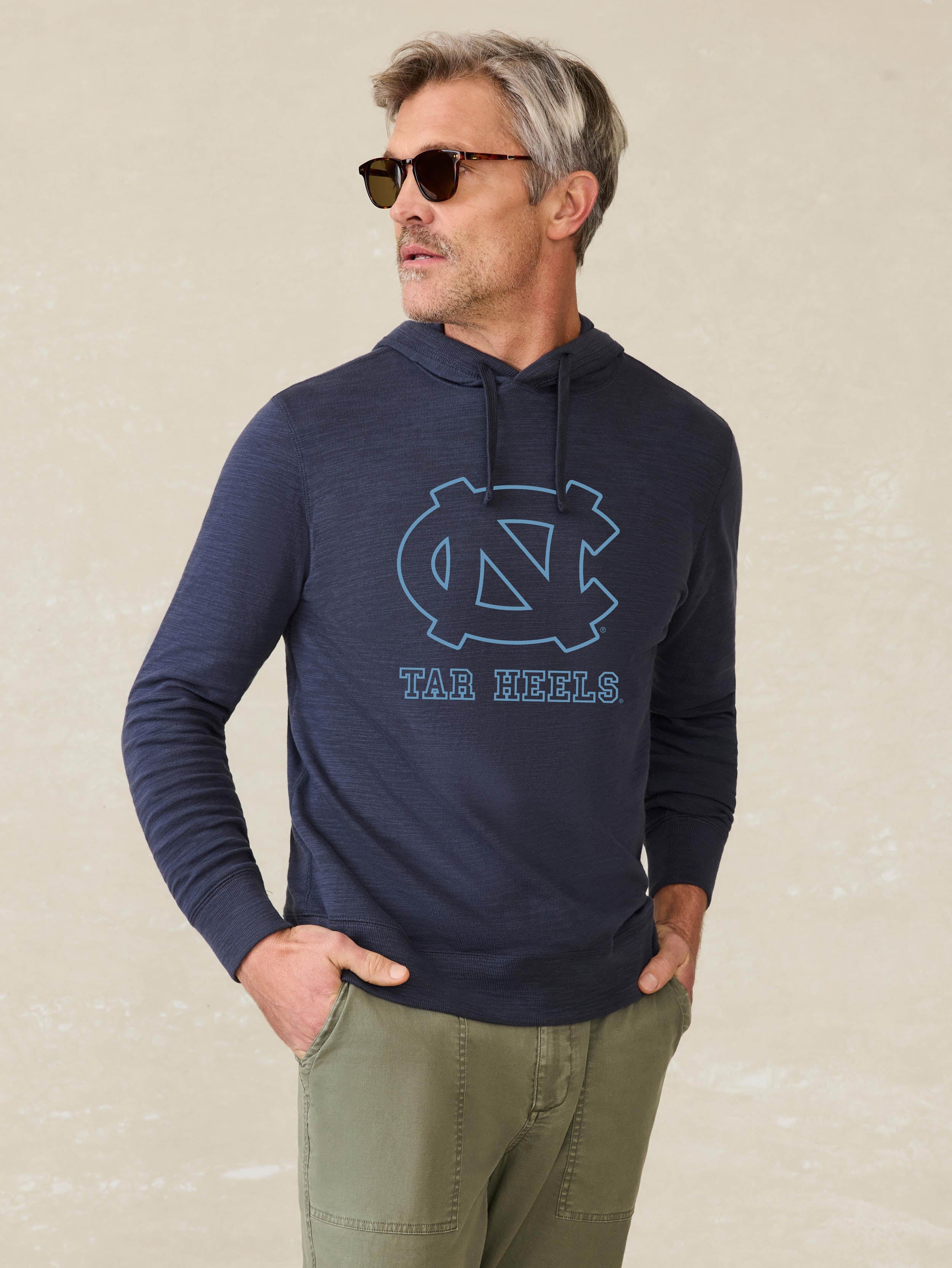 Man is wearing a navy blue hoodie with UNC graphic at the center chest against a beige background