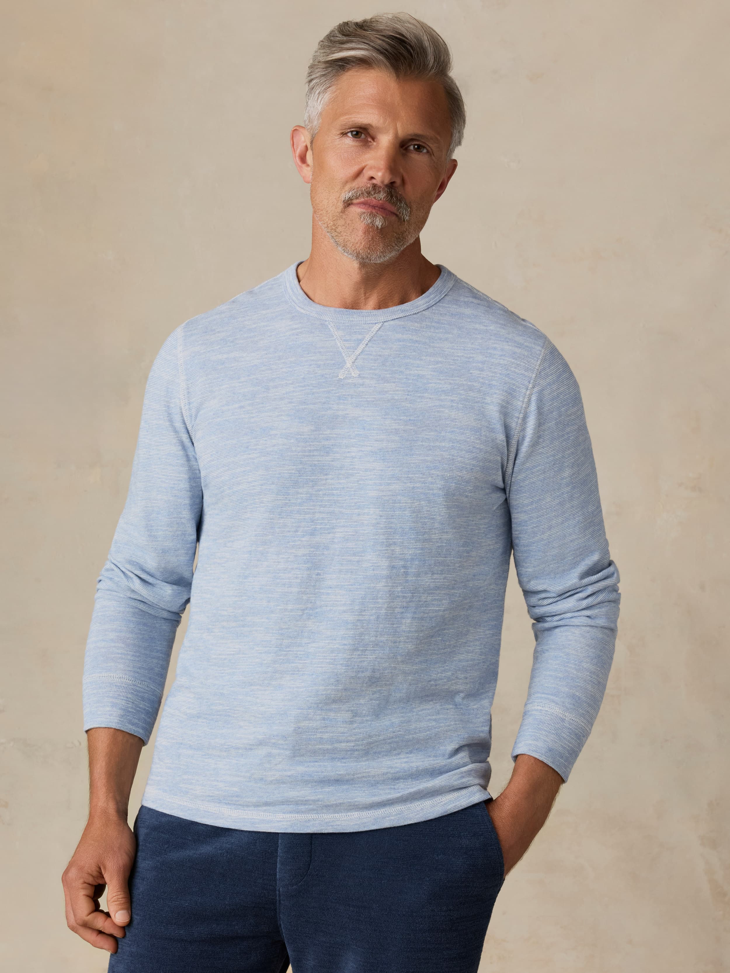 Man wearing a light blue crewneck against a beige background