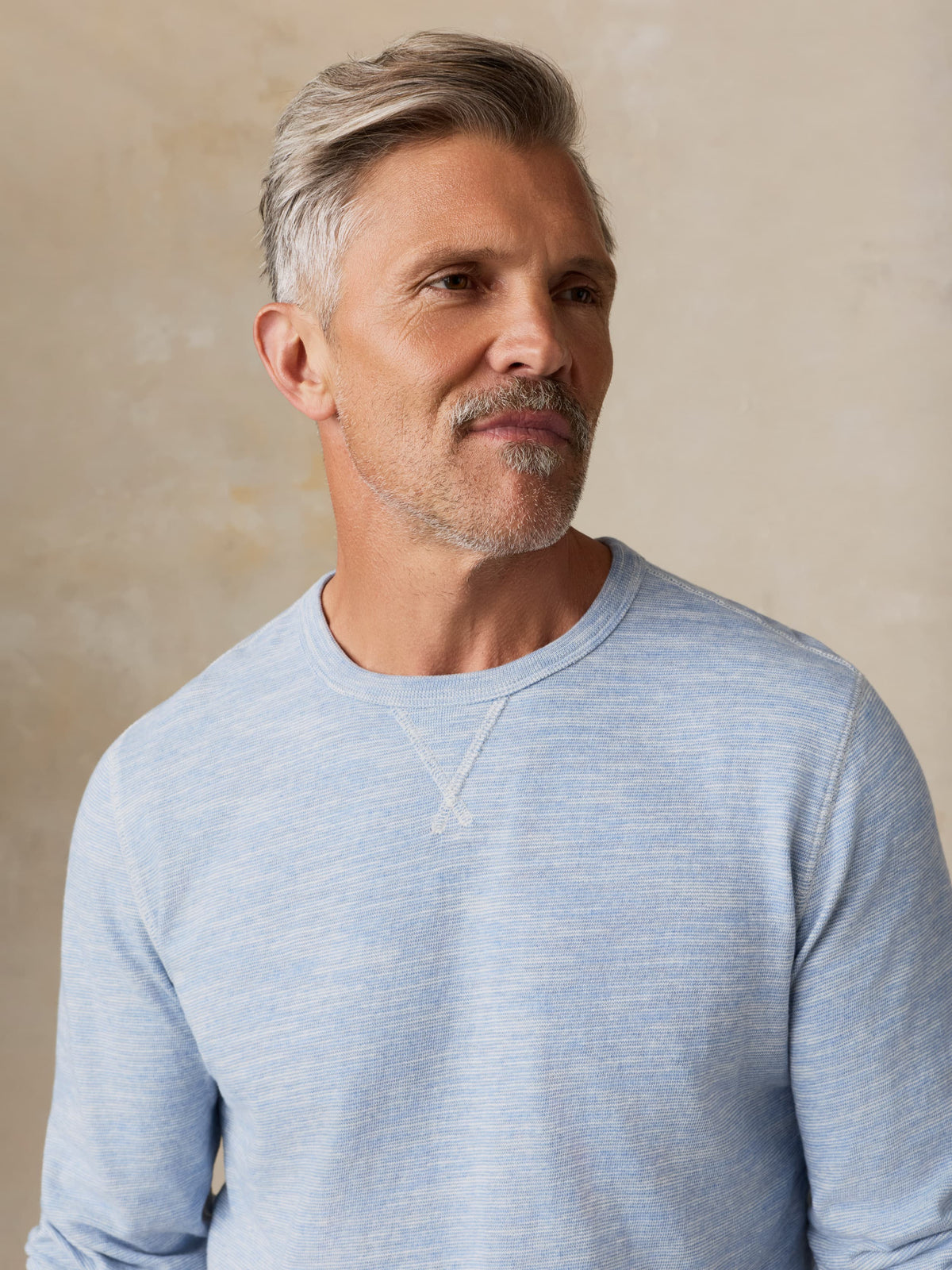 Man wearing a light blue crewneck against a beige background, image 7 of 7