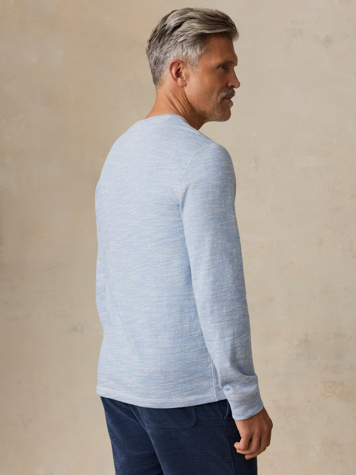 Man wearing a light blue crewneck against a beige background, image 6 of 7
