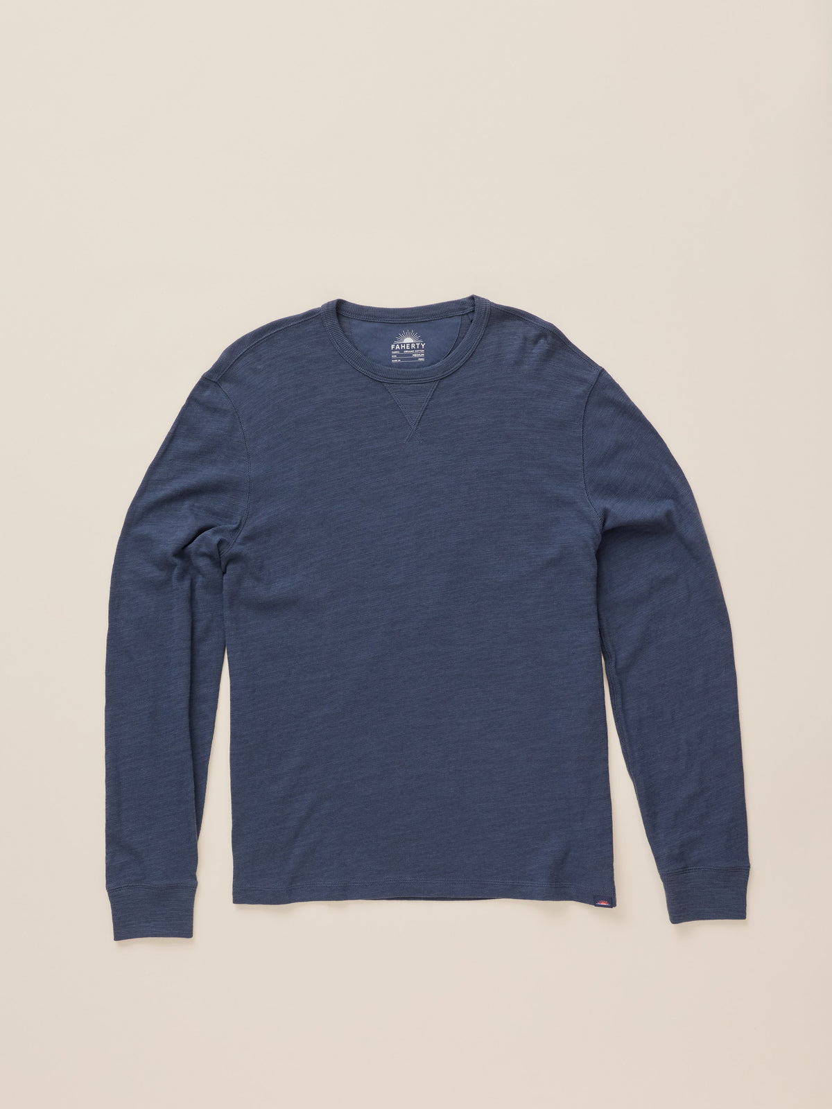 A navy blue long-sleeve crewneck shirt laid flat against a light beige background., image 7 of 8