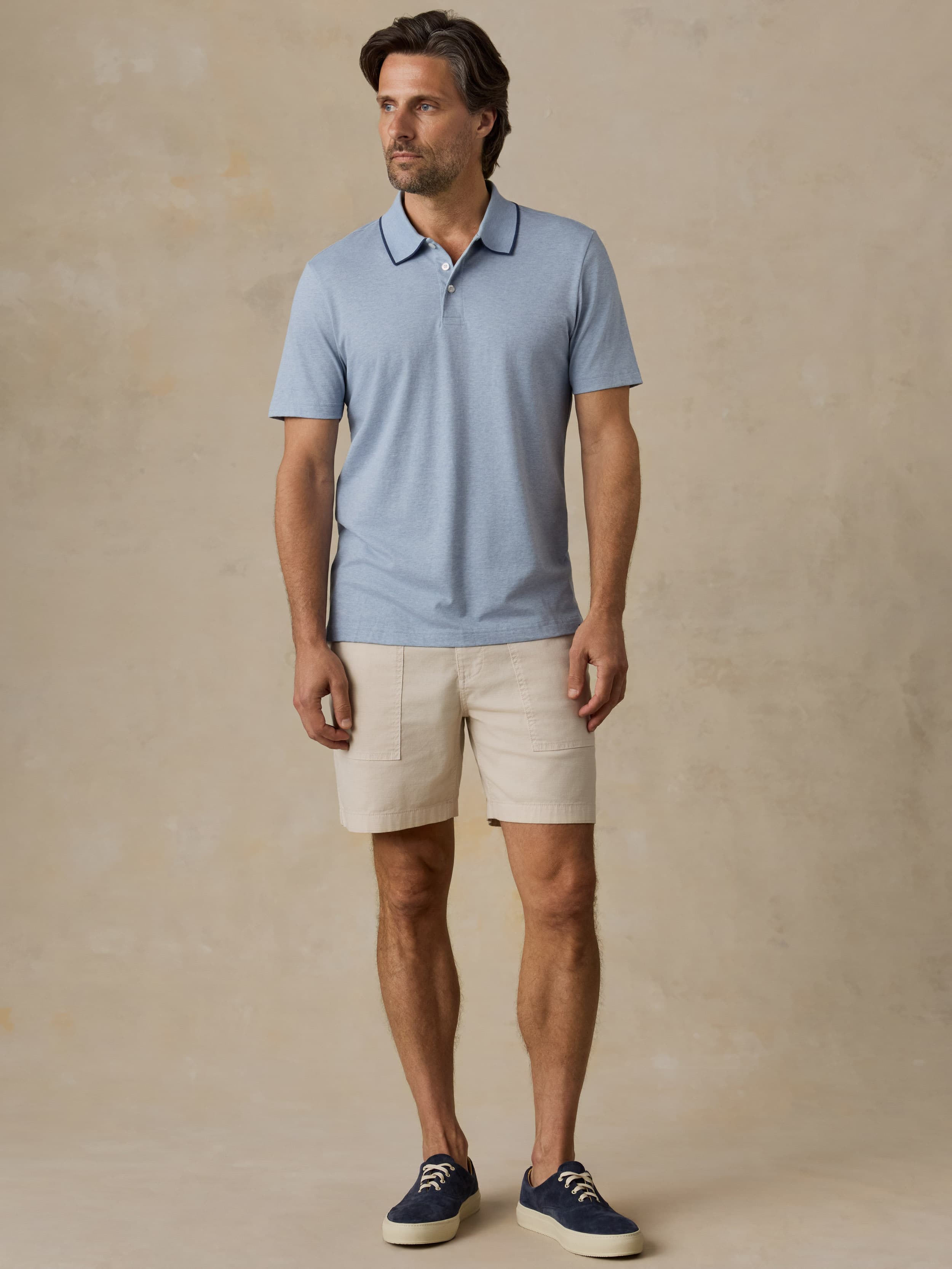 Man wearing a light blue polo shirt and beige shorts against a beige background