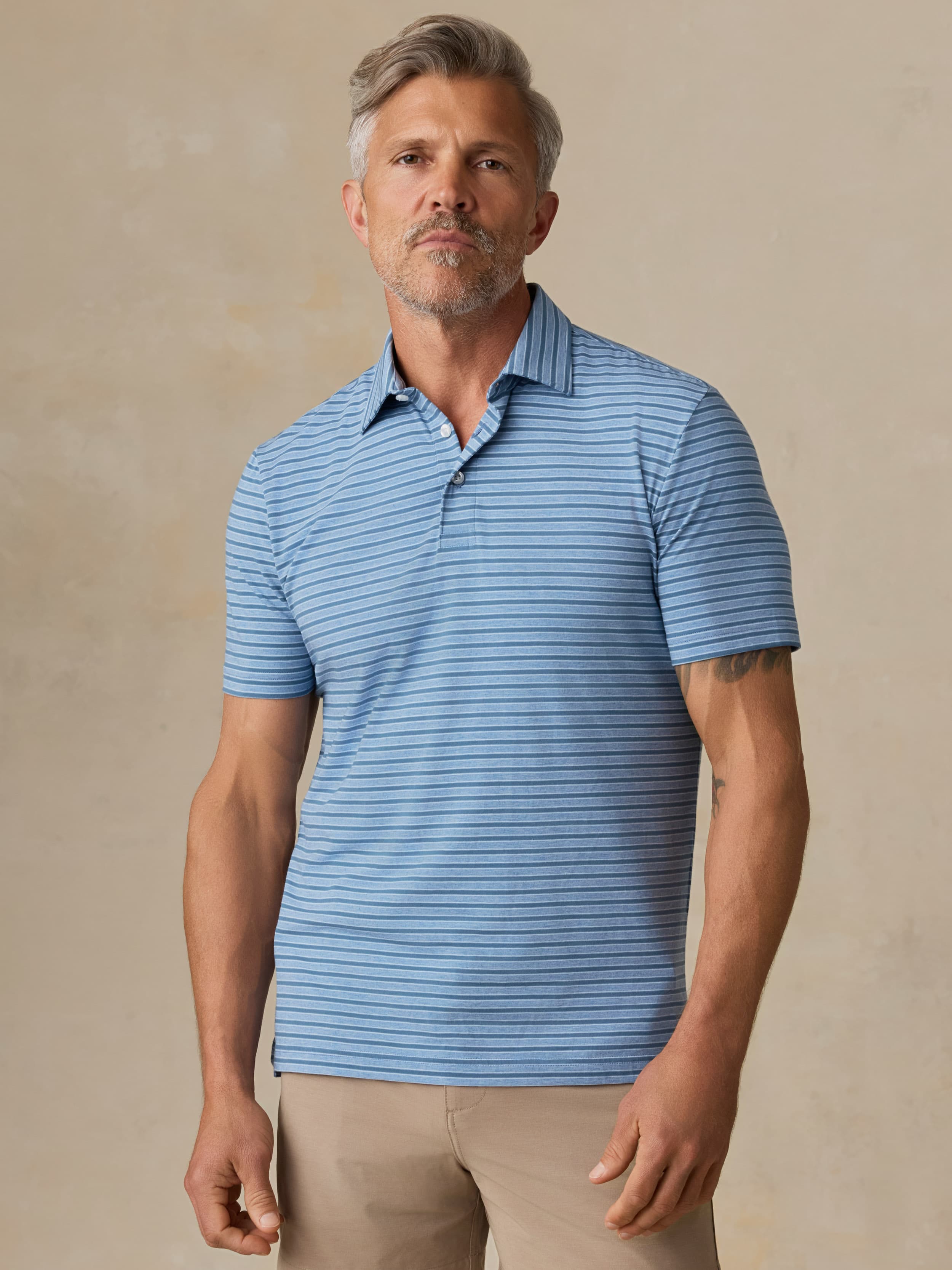 Man wearing a blue striped polo and beige shorts against a beige background