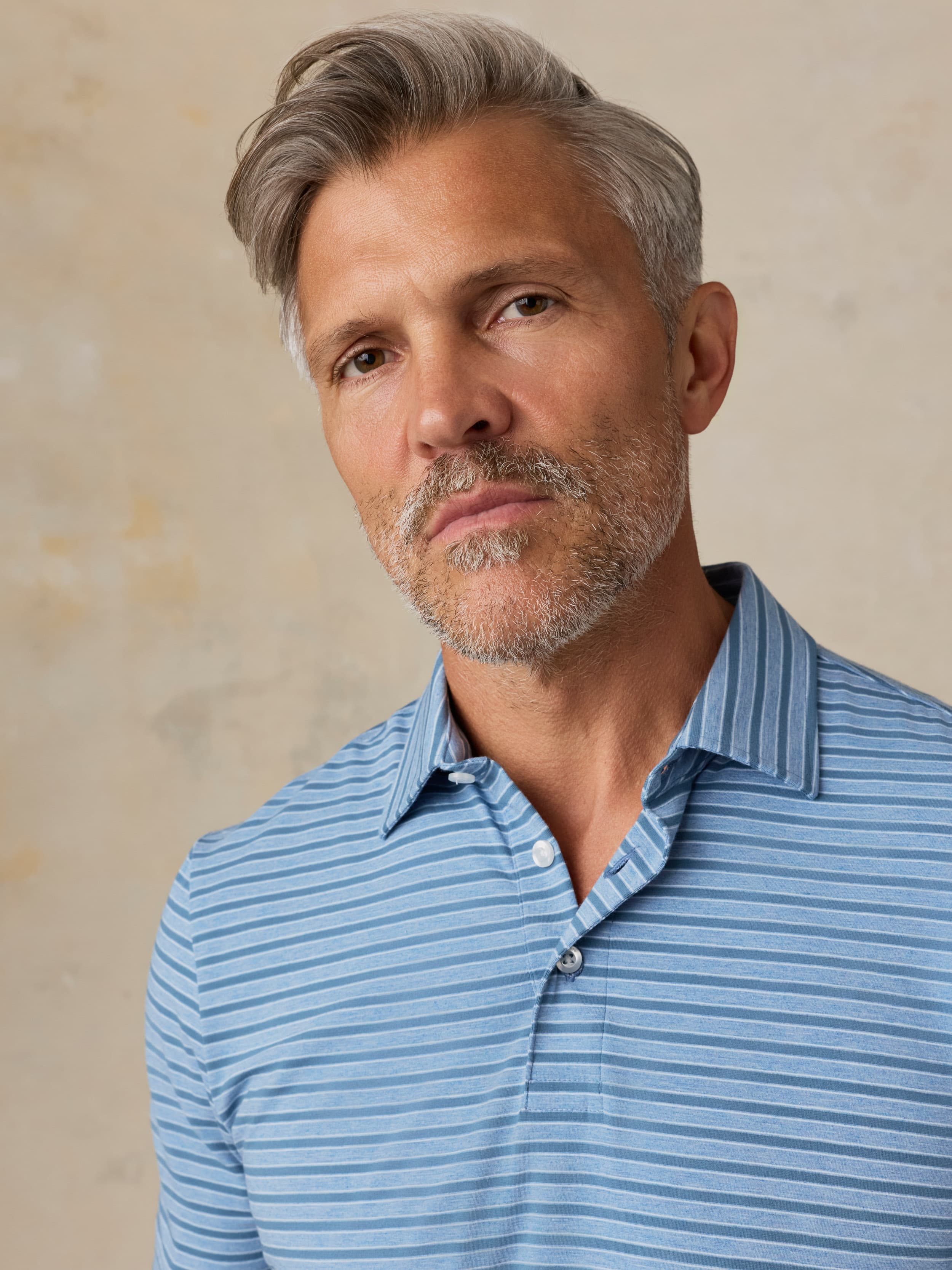 Man wearing a blue striped polo against a beige background