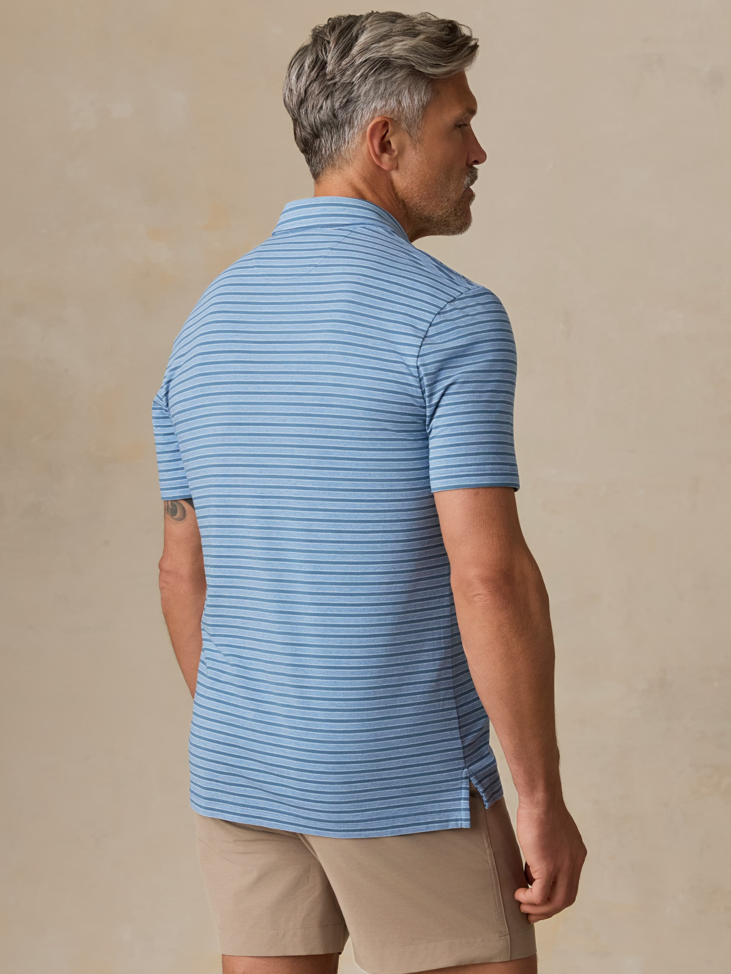 Man wearing a blue striped polo and beige shorts against a beige background