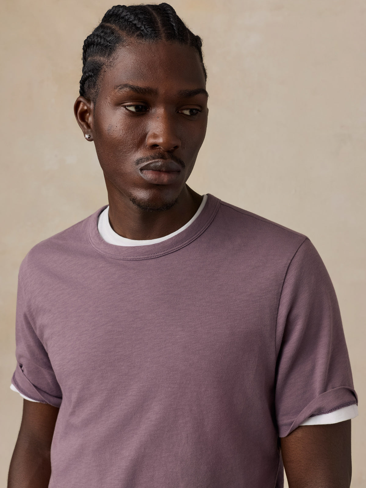 A man wearing a dusty mauve short-sleeve t-shirt set against a textured beige background., image 2 of 6