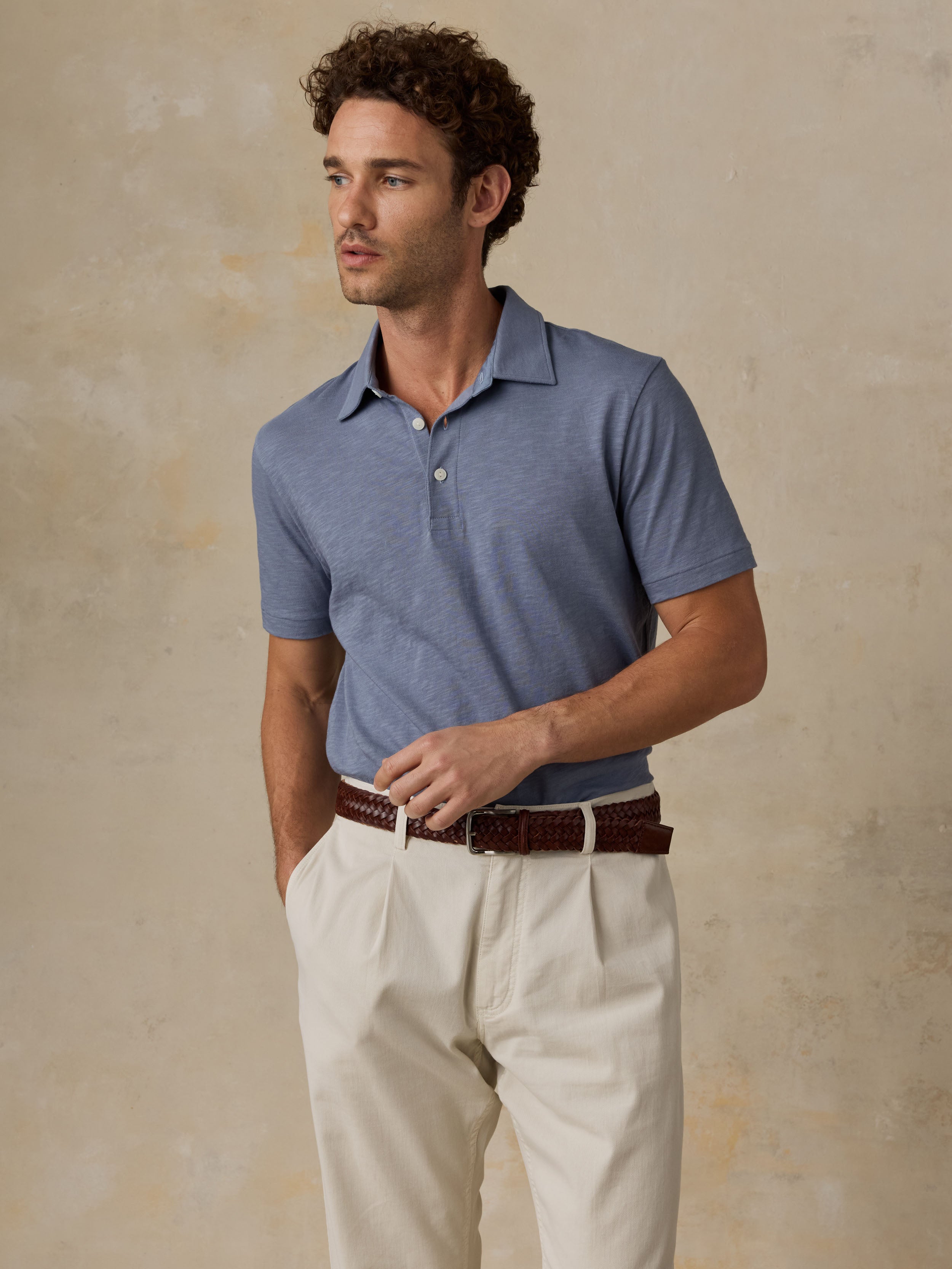 Man wearing a blue polo shirt and beige pants against a beige background