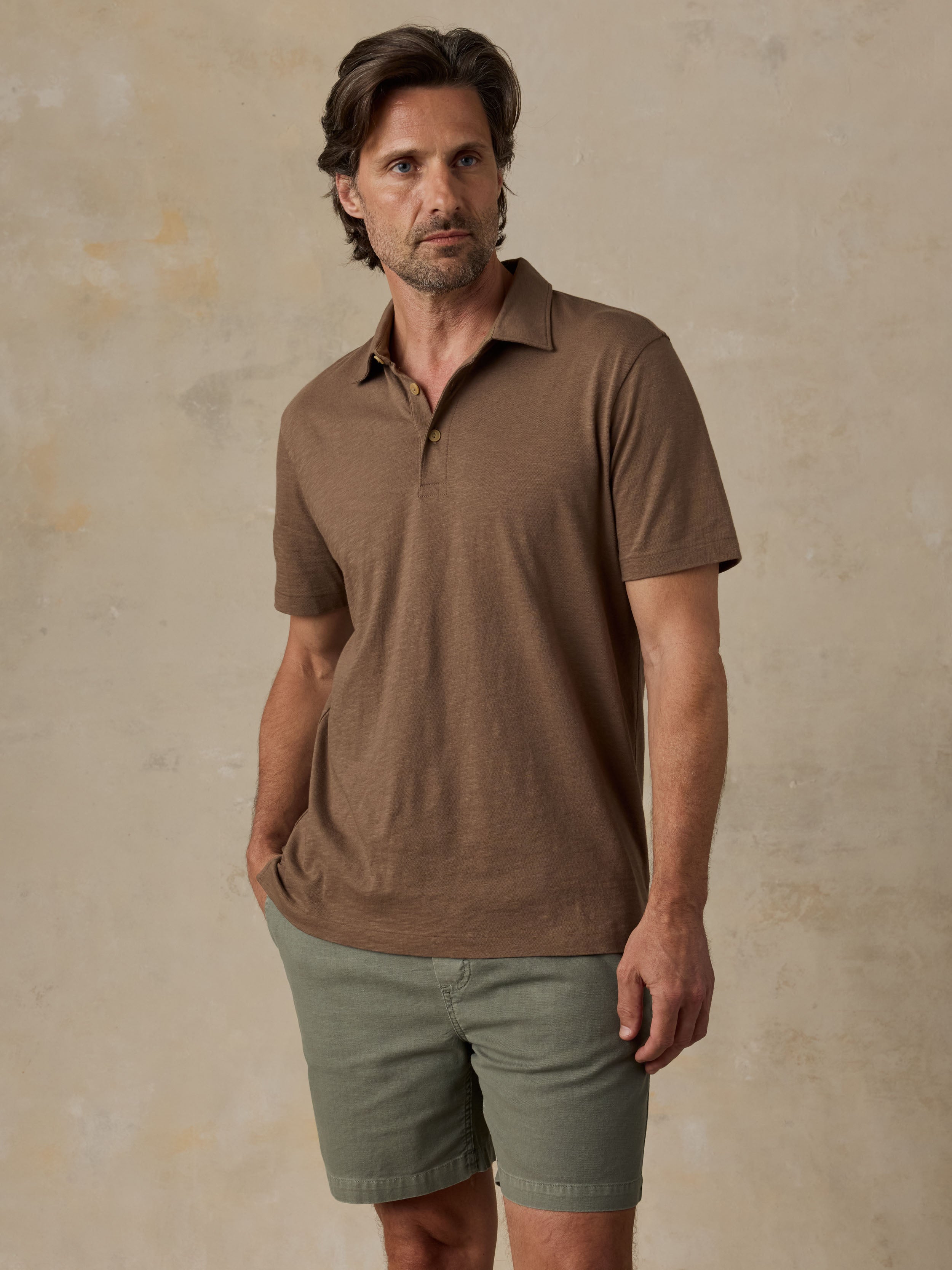 Man wearing a brown polo shirt and green shorts against a beige background
