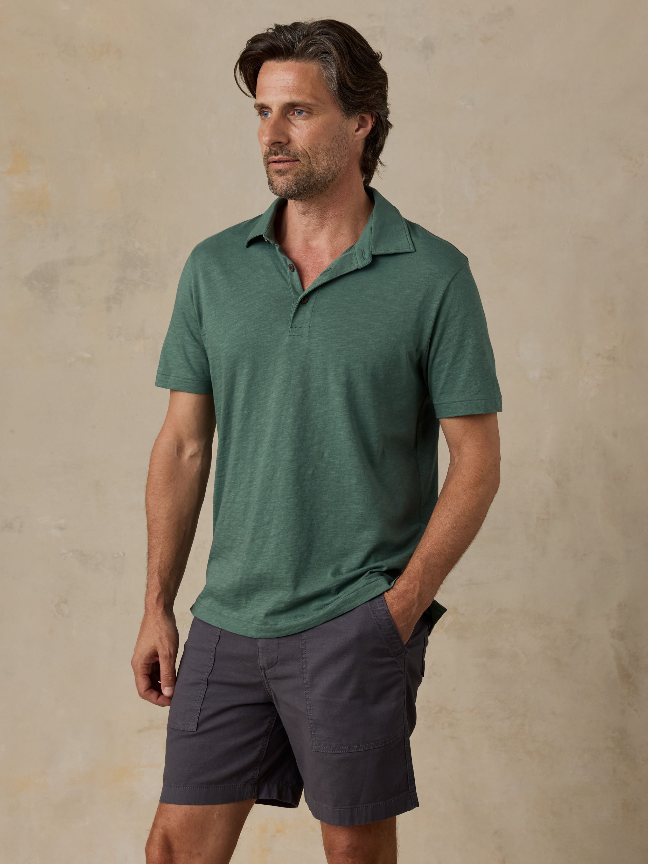 Man wearing a green polo shirt and dark shorts against a beige background