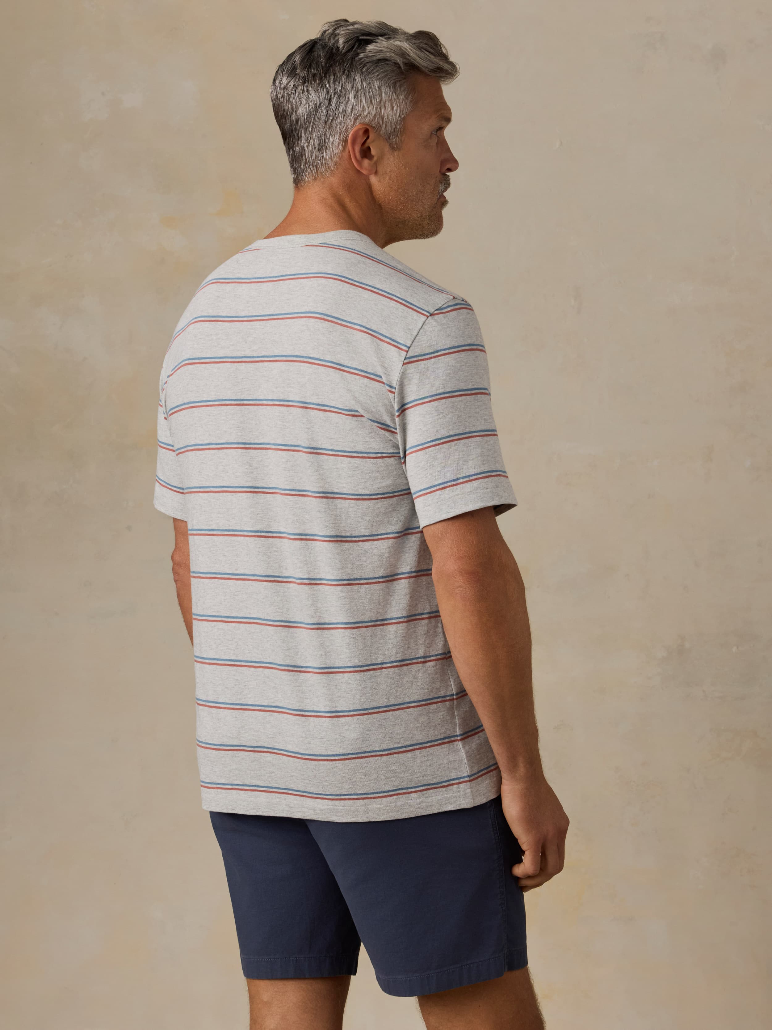 Man wearing a striped t-shirt and navy shorts against a beige background