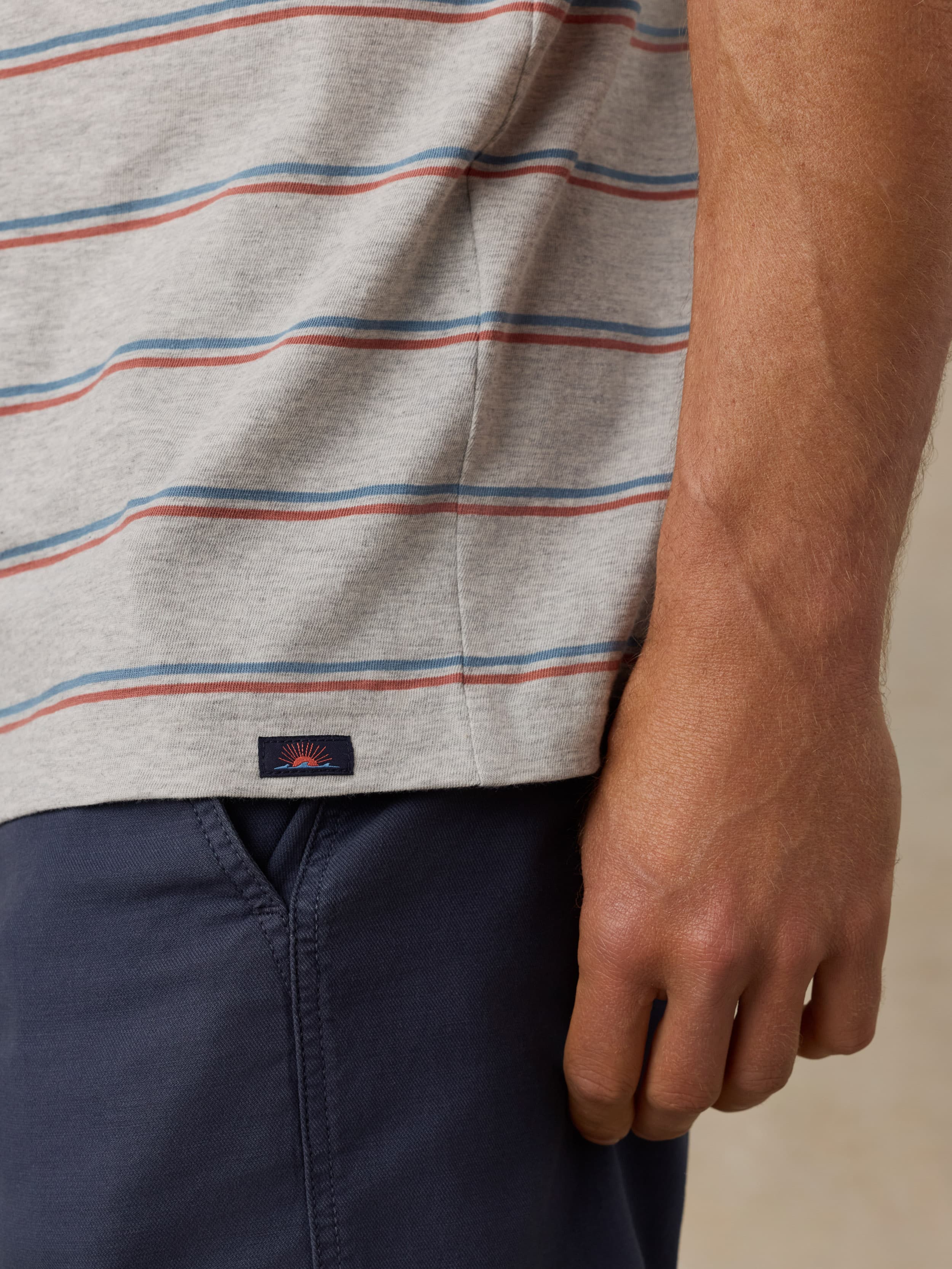 Close-up of a man wearing a striped shirt with a Faherty brand logo and navy shorts on a beige background