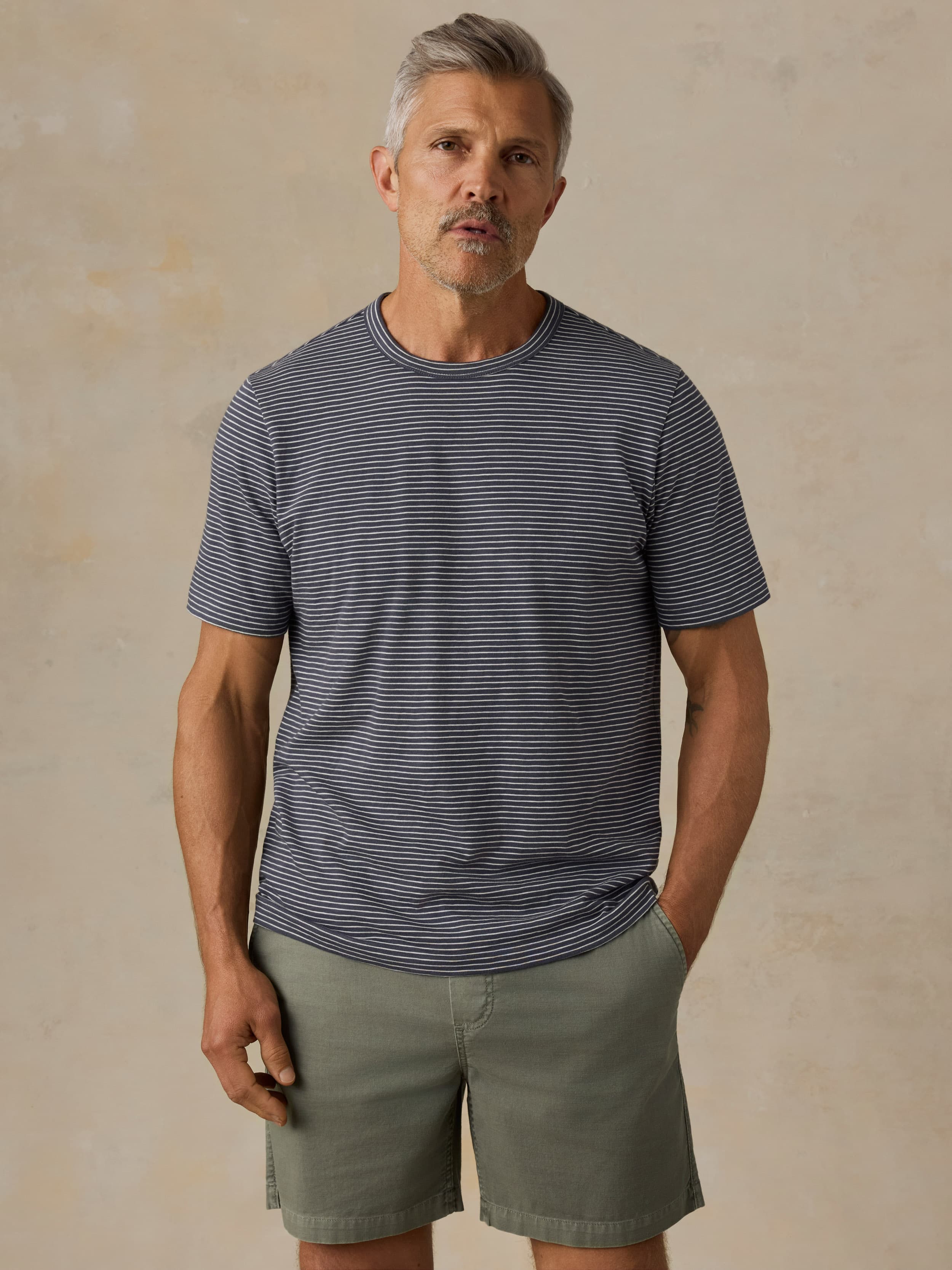Man wearing blue striped shirt and green shorts against a beige background