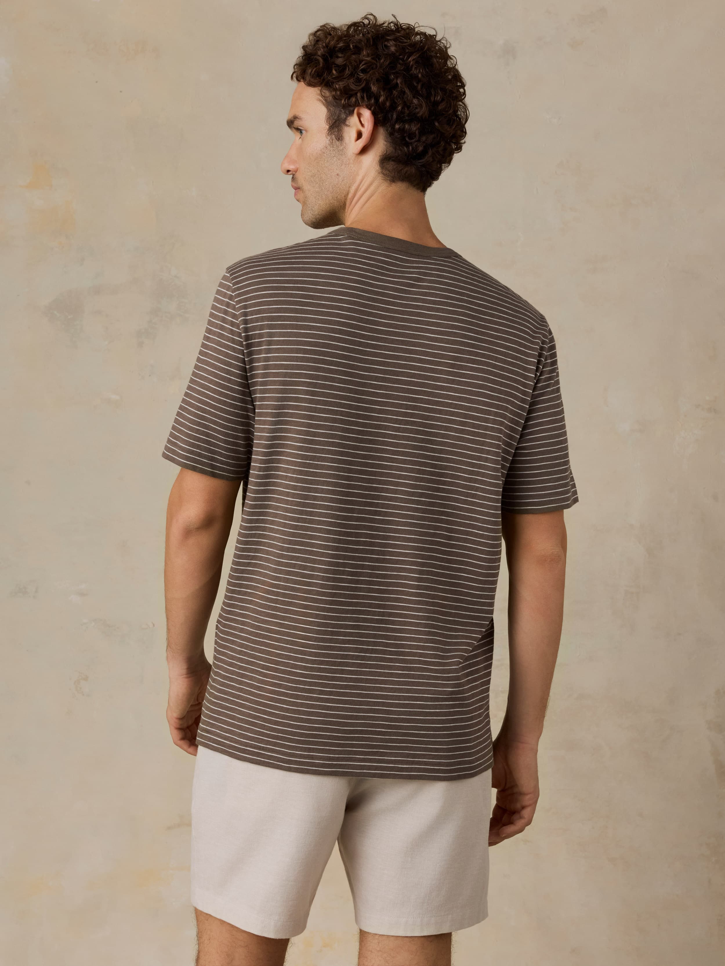 Man wearing a brown striped t-shirt and beige shorts against a beige background