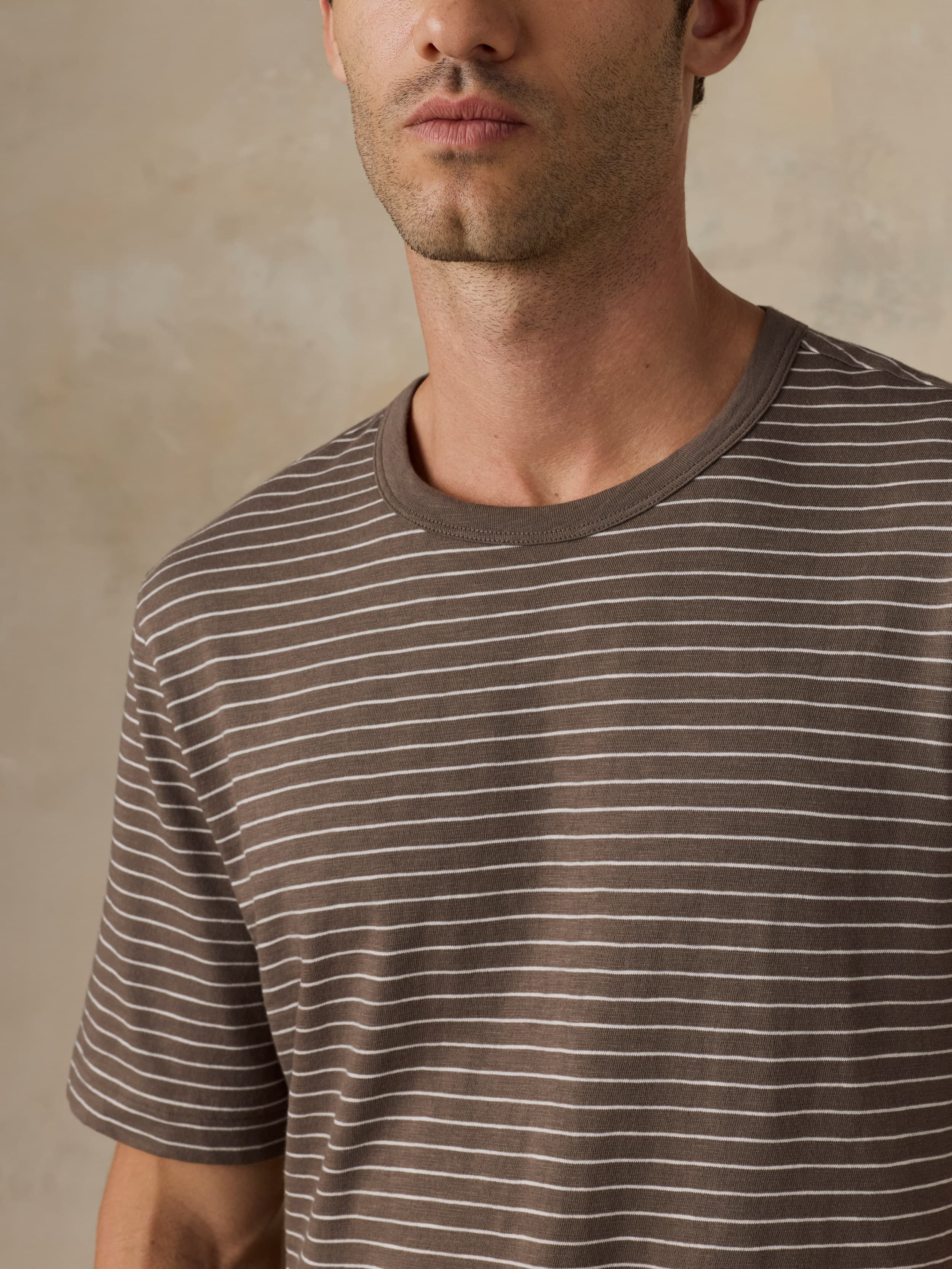 Man wearing a brown striped t-shirt against a beige background