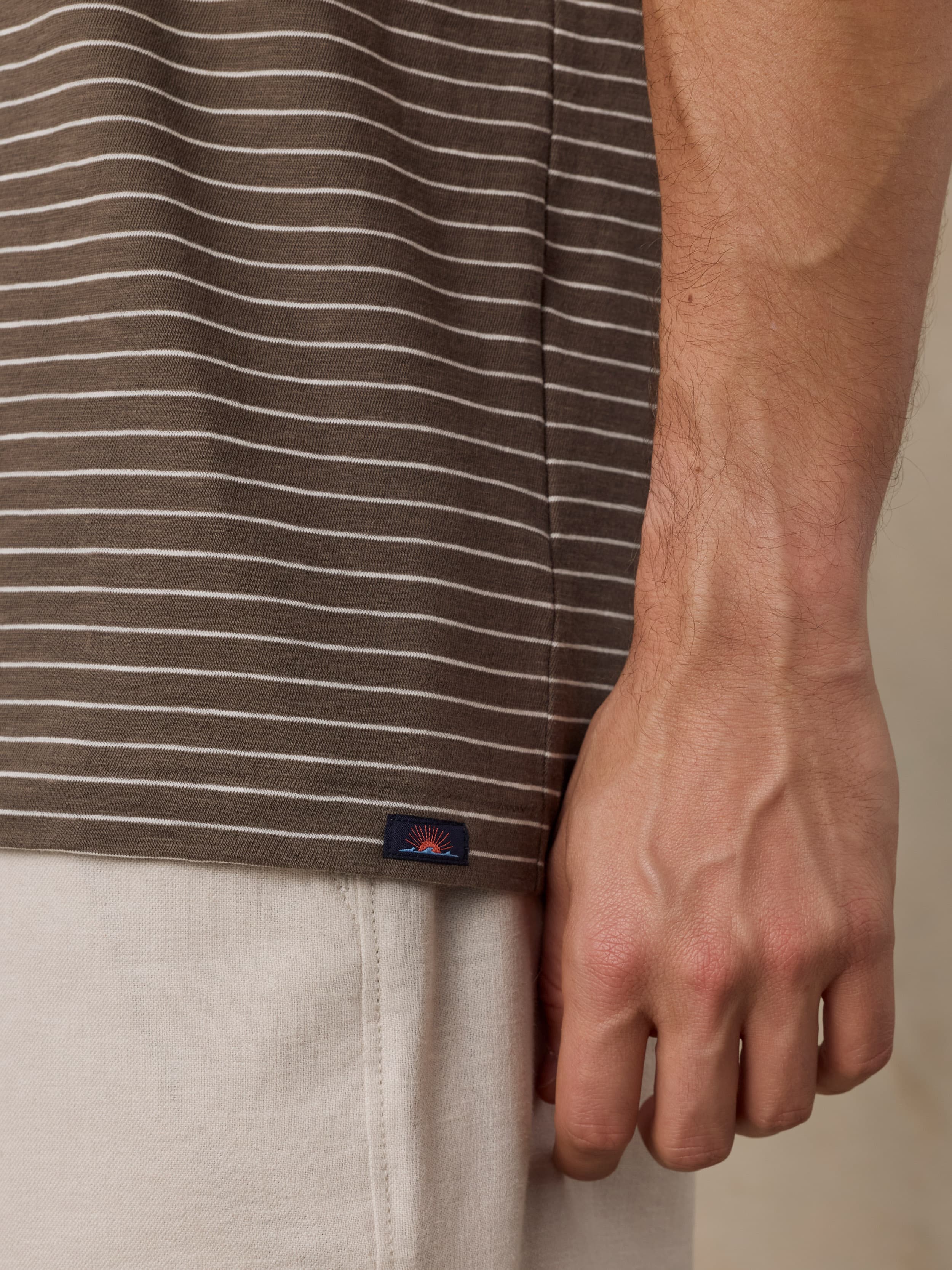 Close-up of a man wearing a brown striped shirt with a Faherty brand logo and beige shorts