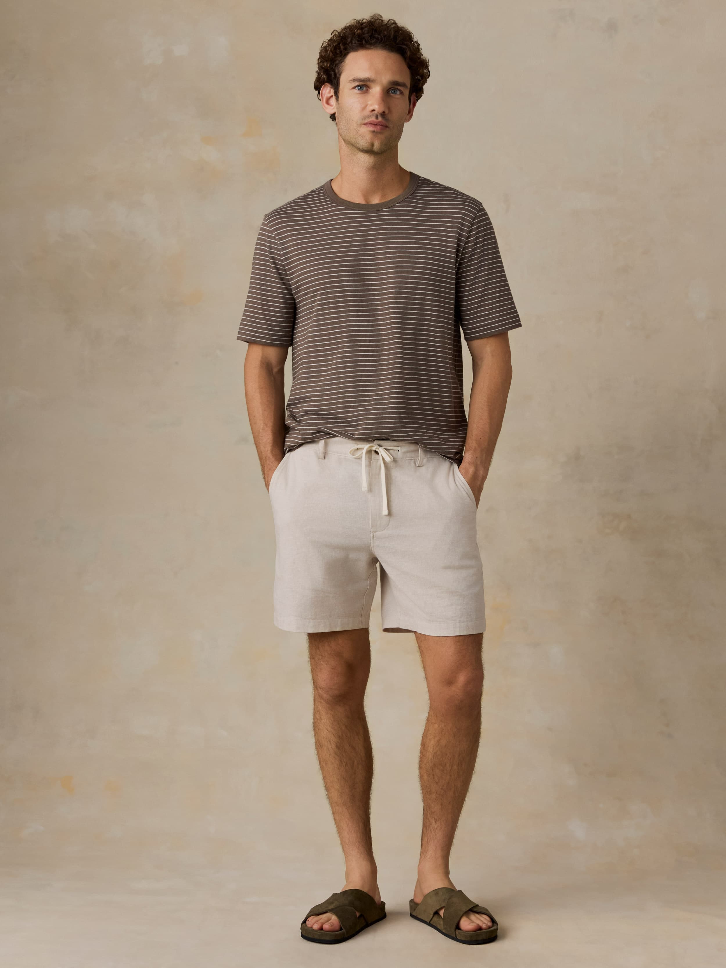 Man wearing a brown striped t-shirt and beige shorts against a beige background