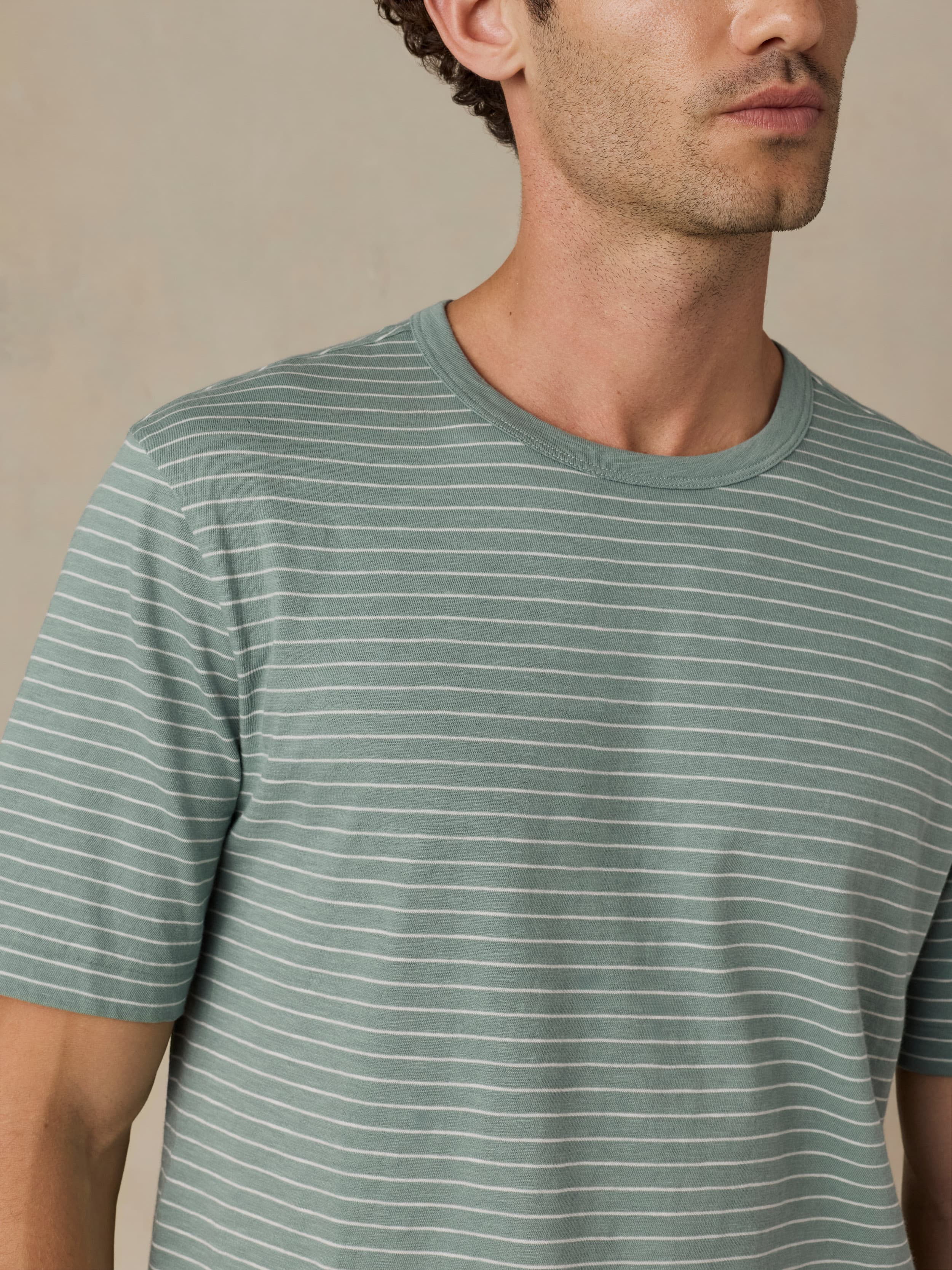 Man wearing a green and white striped tee against a beige background