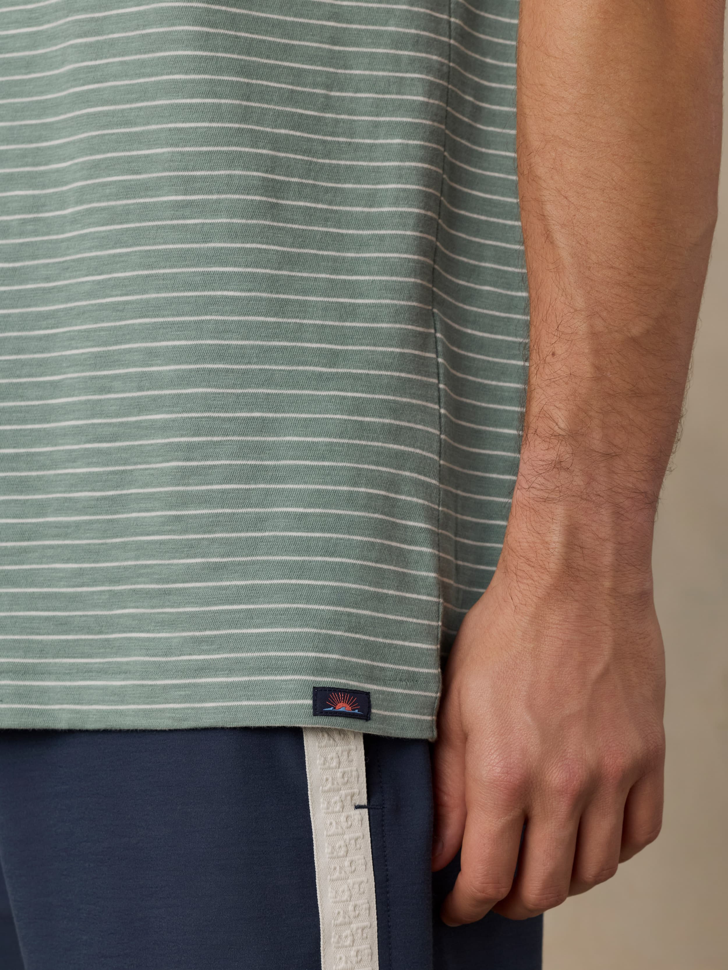 Man wearing a green and white striped tee with navy swim shorts against a beige background