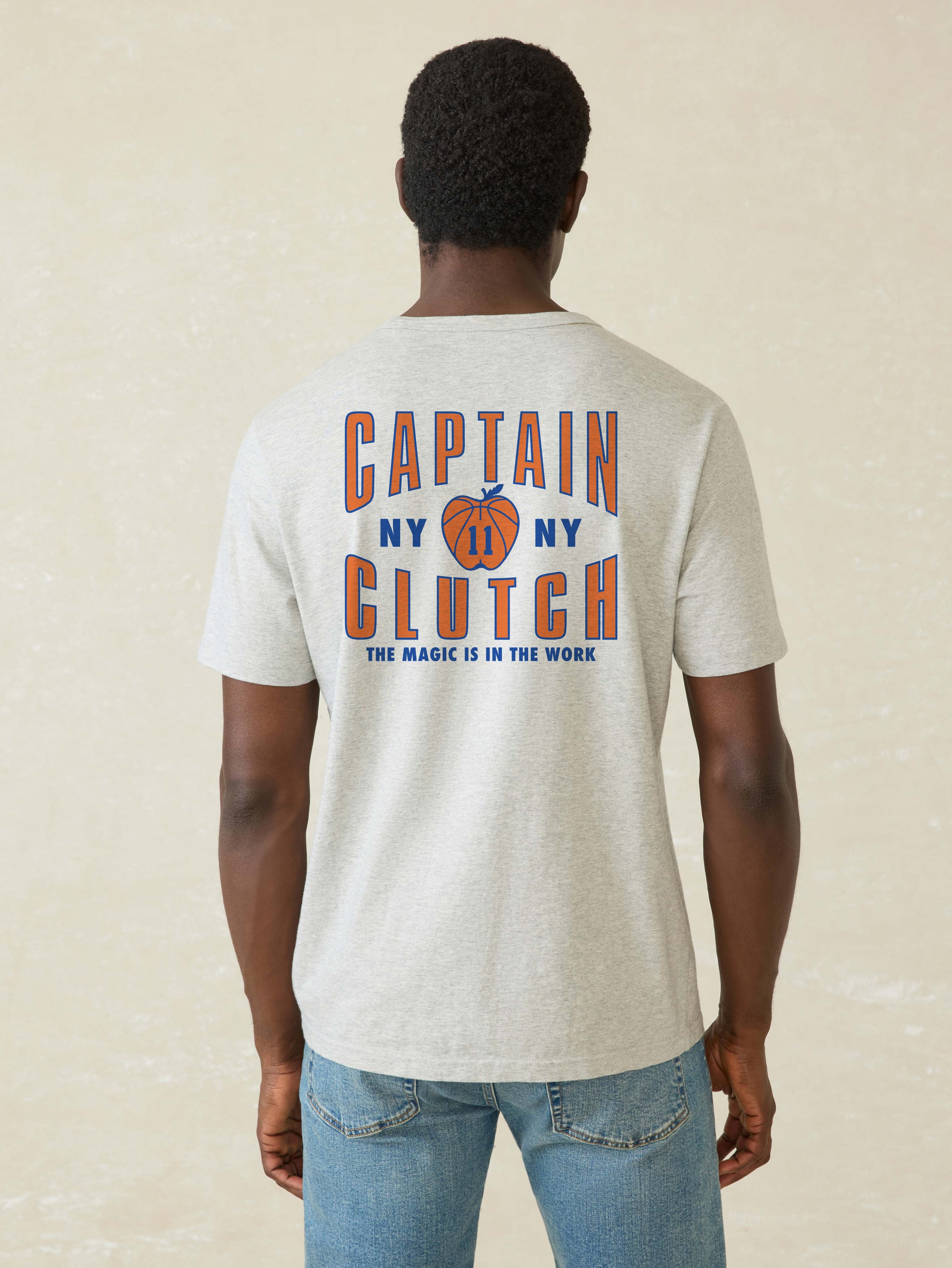 Man wearing a t-shirt with 'Captain Clutch' text on the back against a beige background